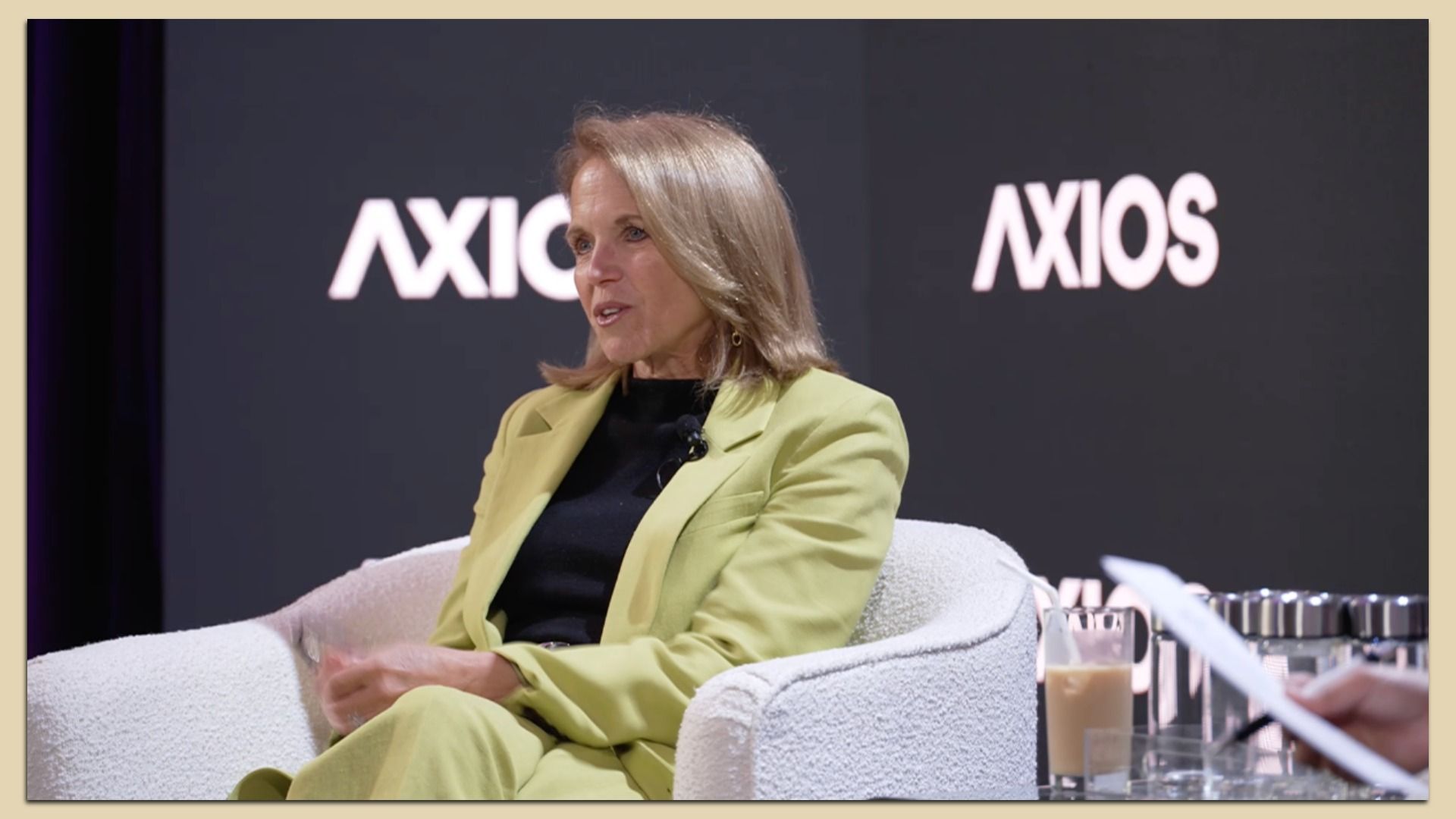 Katie Couric sits in yellow suit on a chair