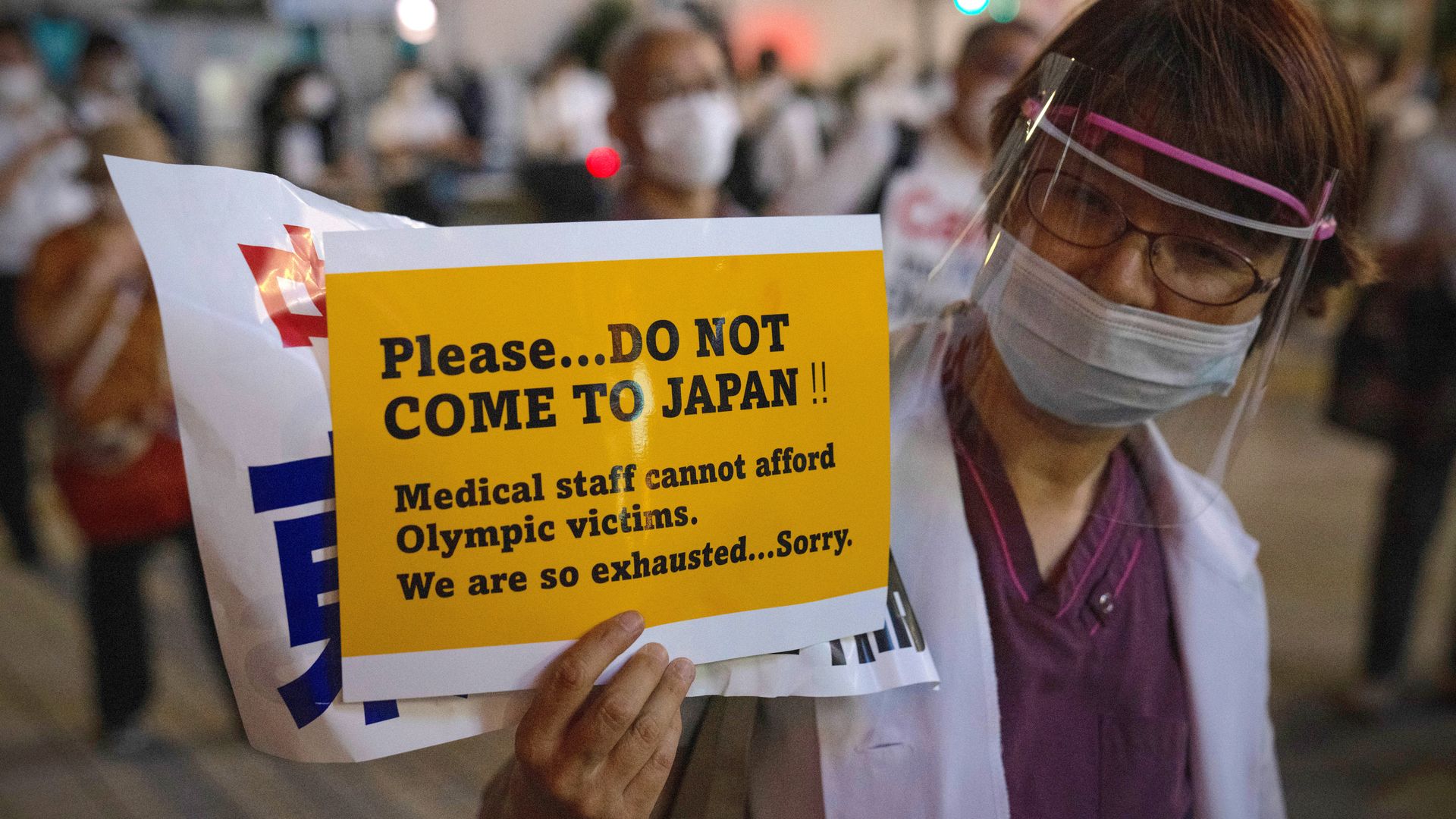 A doctor holds up a poster asking people not to come to Japan for the Olympics.