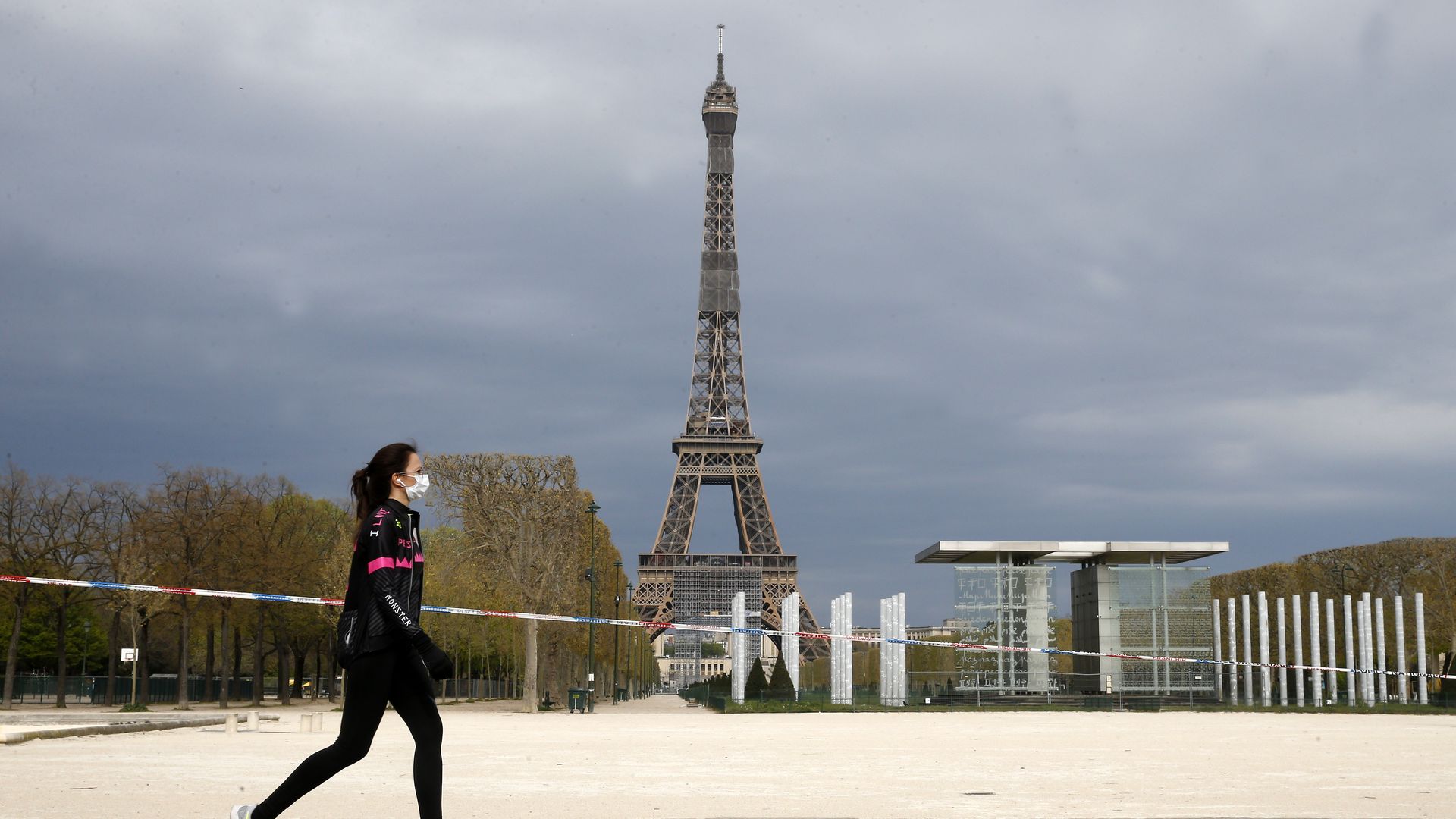 A person walking in front of the eiffel tower with a mask on.