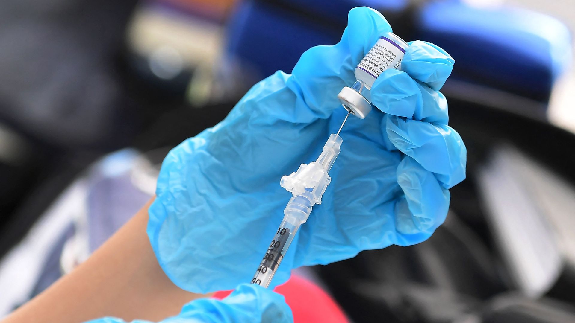 Picture of hands wearing medical gloves holding the Pfizer vaccine and filling up a syringe