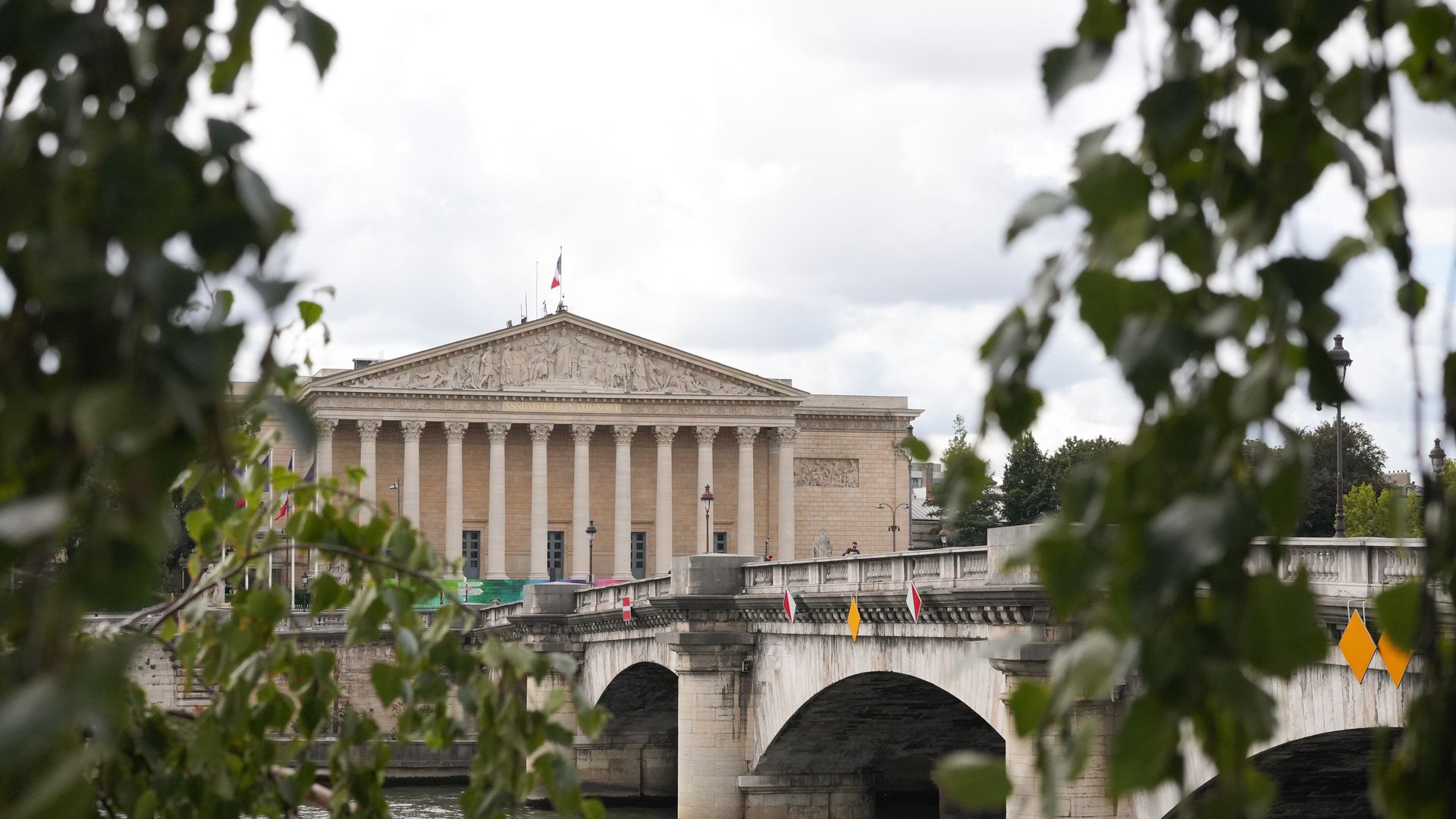 The National Assembly building in Paris, framed by plants on either side in the foreground.