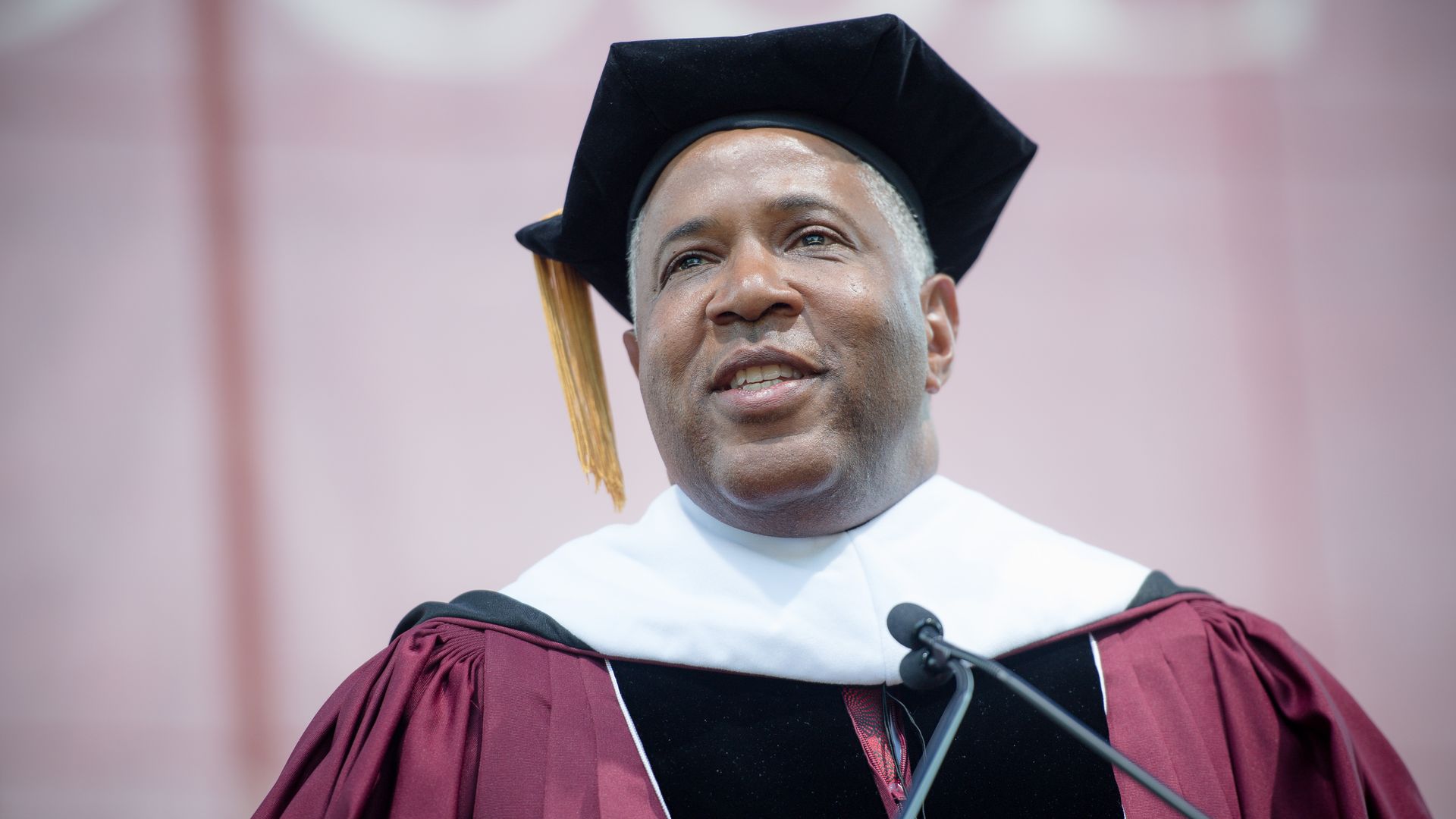 In this image, Robert Smith stands in a cap and gown for a commencement speech in front of a microphone