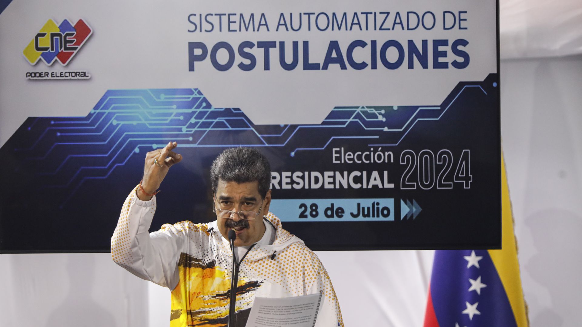 Venezuela President Nicolas Maduro has his arm up and his hand out while speaking behind a microphone 
