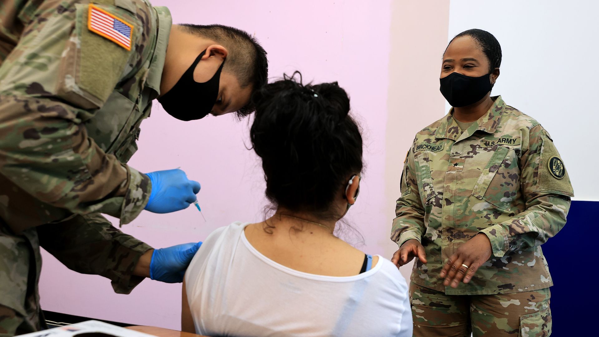A woman receives a shot of the Moderna coronavirus vaccine by a soldier in Army fatigues 