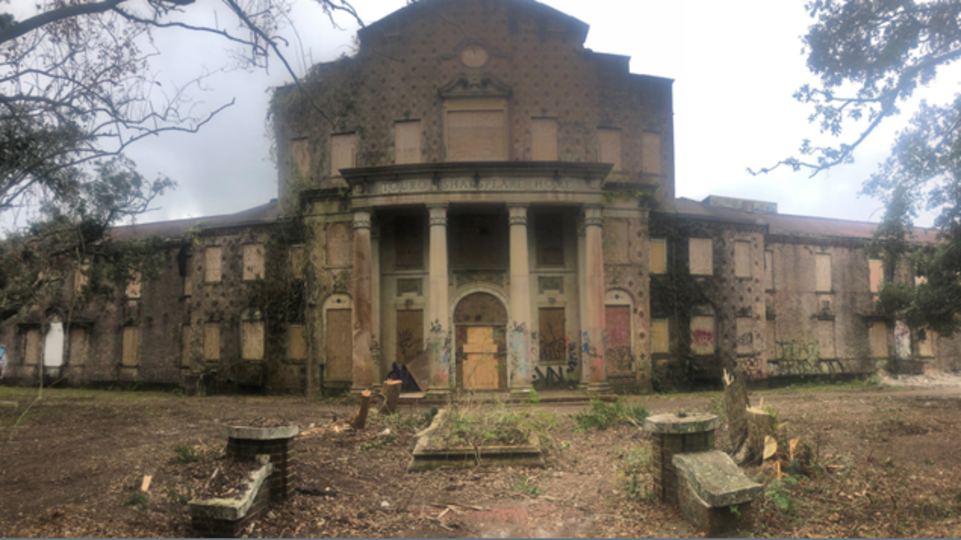 An old, blighted building with columns at the front. Its windows and doors are boarded over.