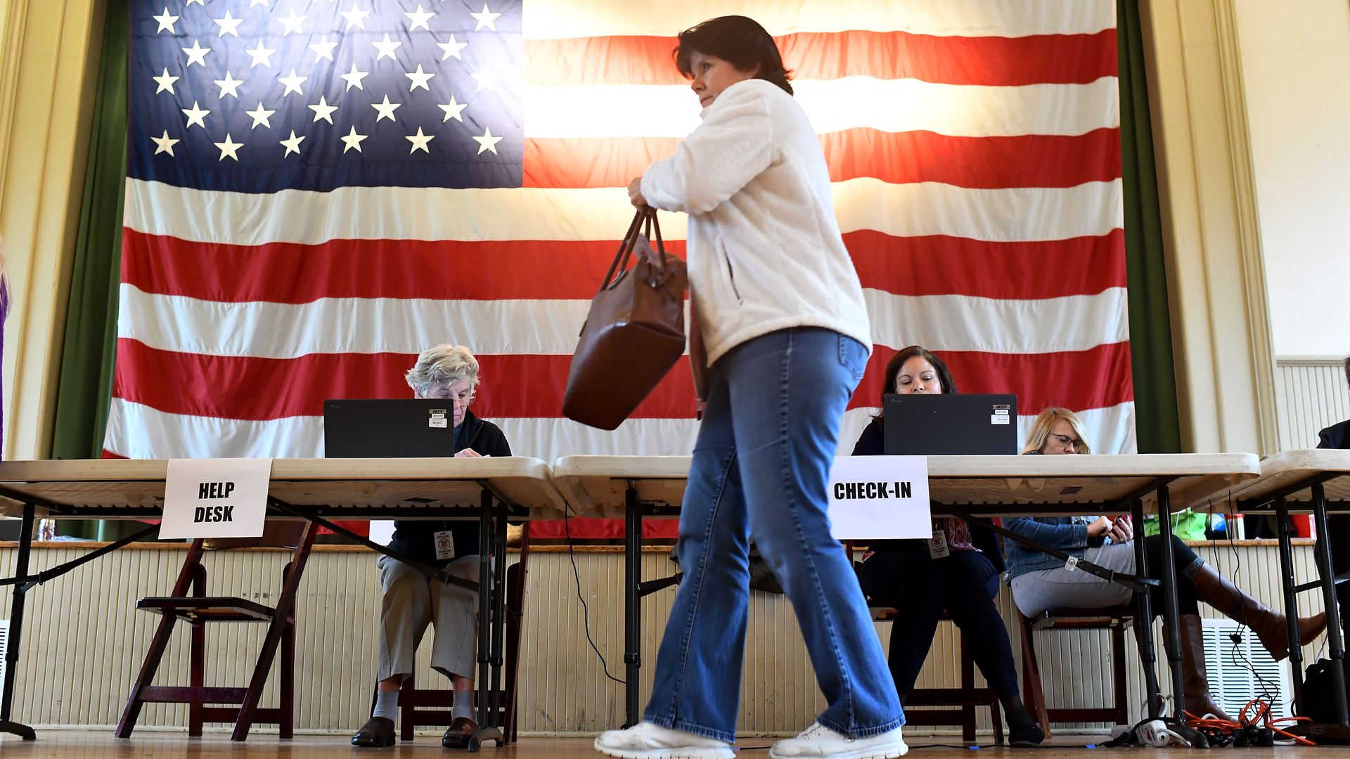 A woman votes in Virginia, with a large American flag lit up behind her as she walks.