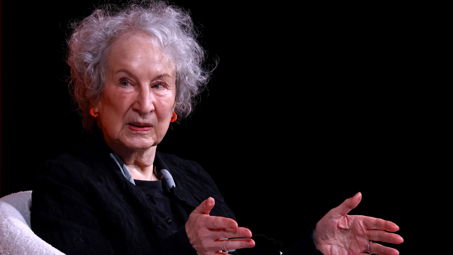 Margaret Atwood, 84, sits in a white chair during an interview with a black background. 
