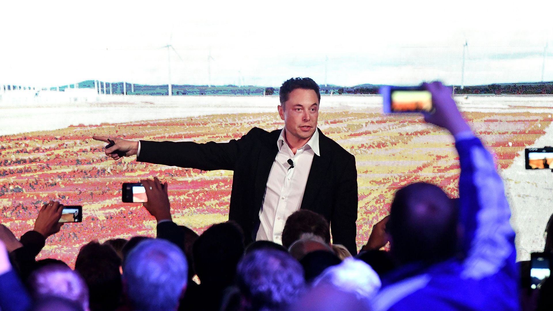 Elon Musk points to his right as people take photos
