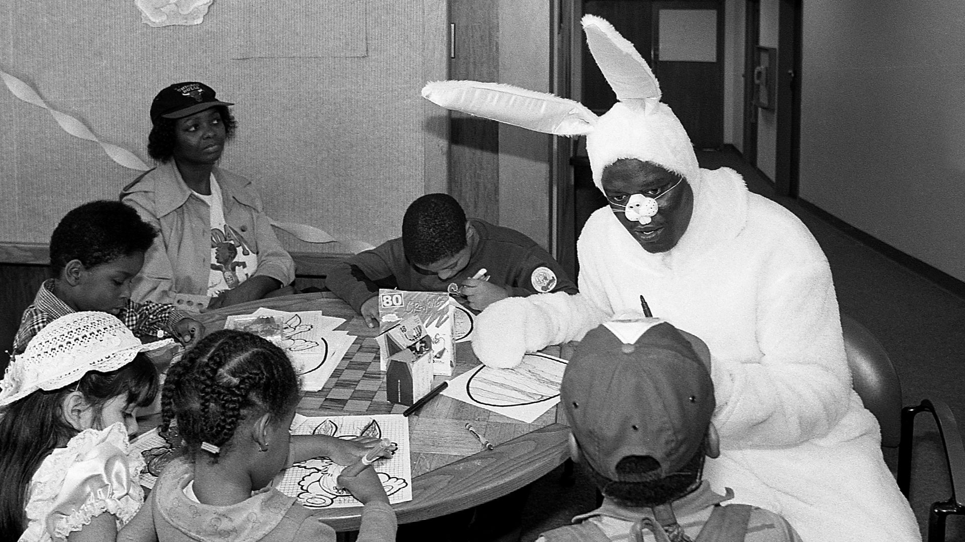 Photo of a man dressed in a bunny costume talking to kids. 