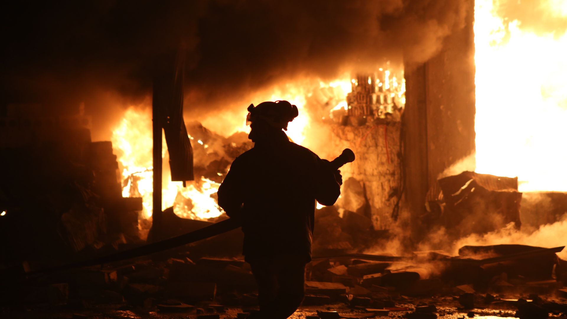Civil defense member in shadows extinguishes fire.