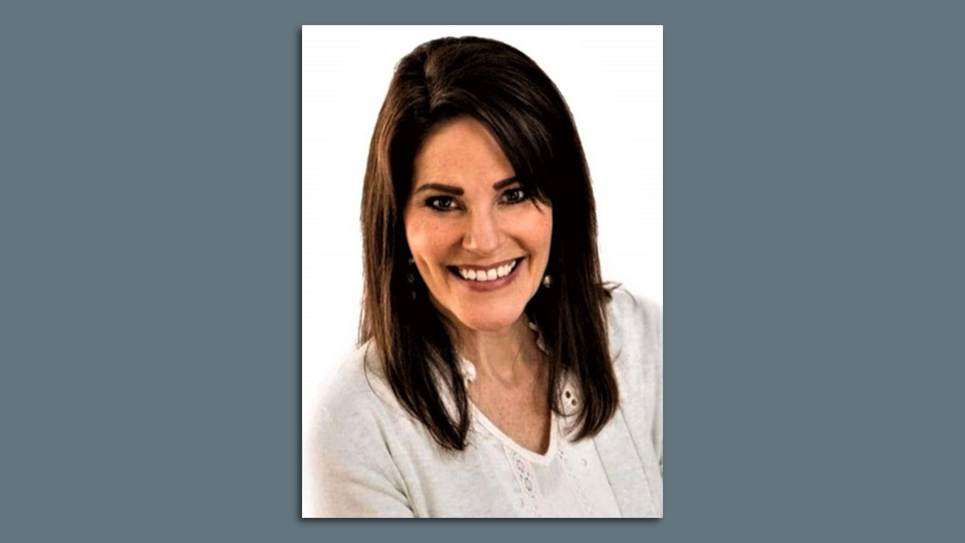 A portrait of a woman in a white shirt with brown hair in front of a white background.