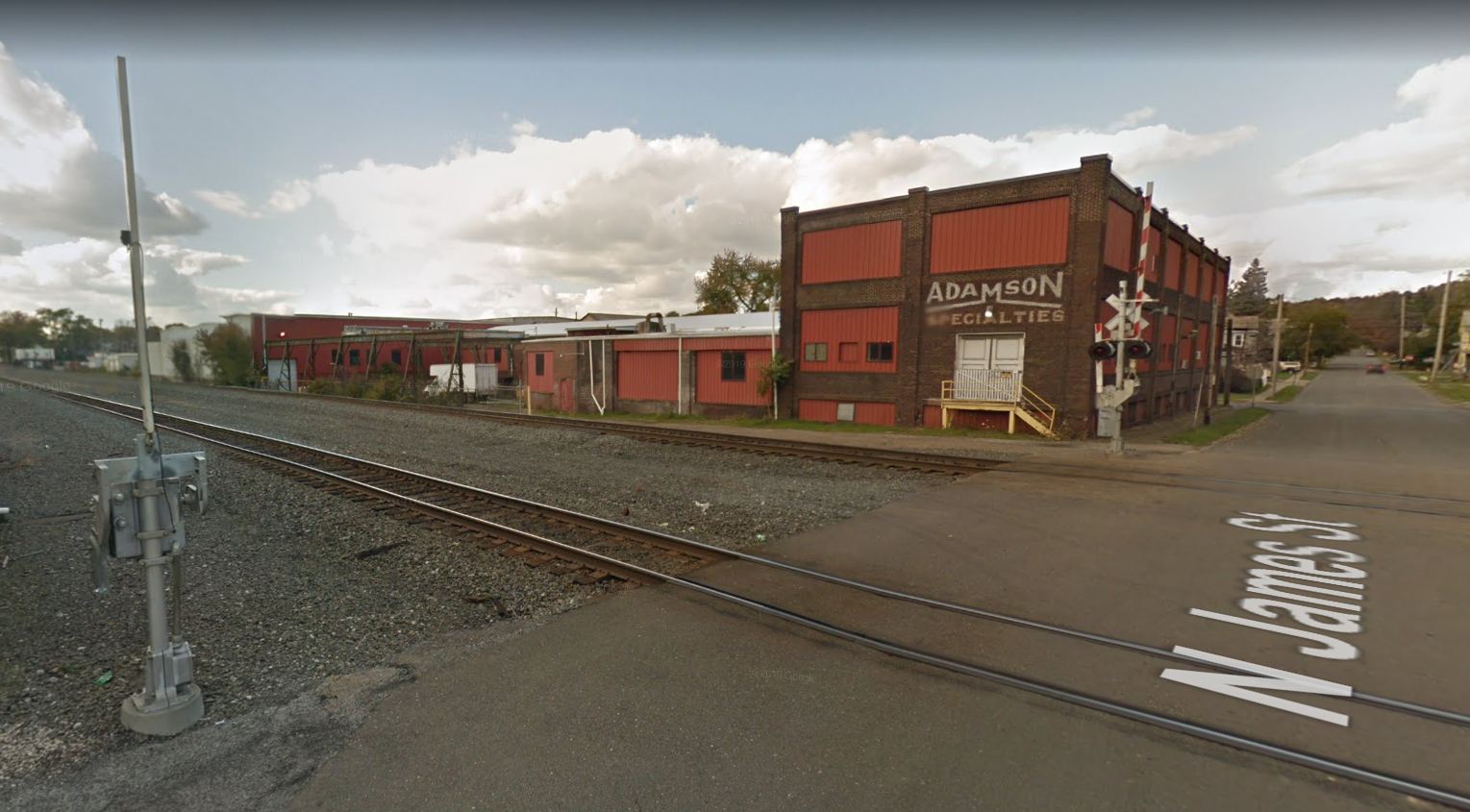 A railroad crossing with a brick factory building in the background. 