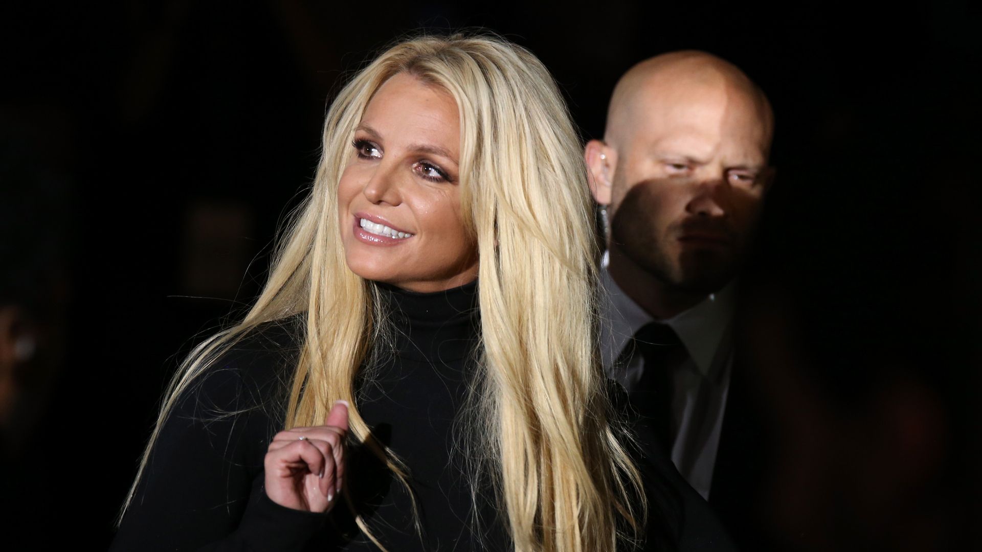 Photo of Britney Spears smiling with a security guard next to her
