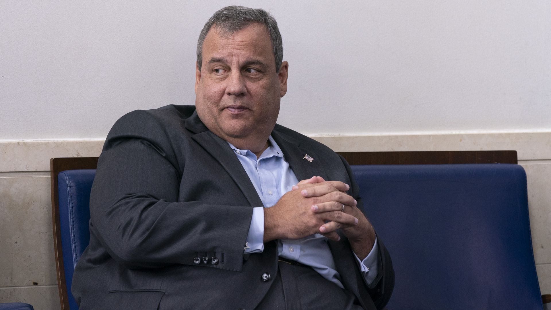Former New Jersey Gov. Chris Christie sits in a blue chair at the White House in 2020 slightly smiling and looking sideways with his hands clasped