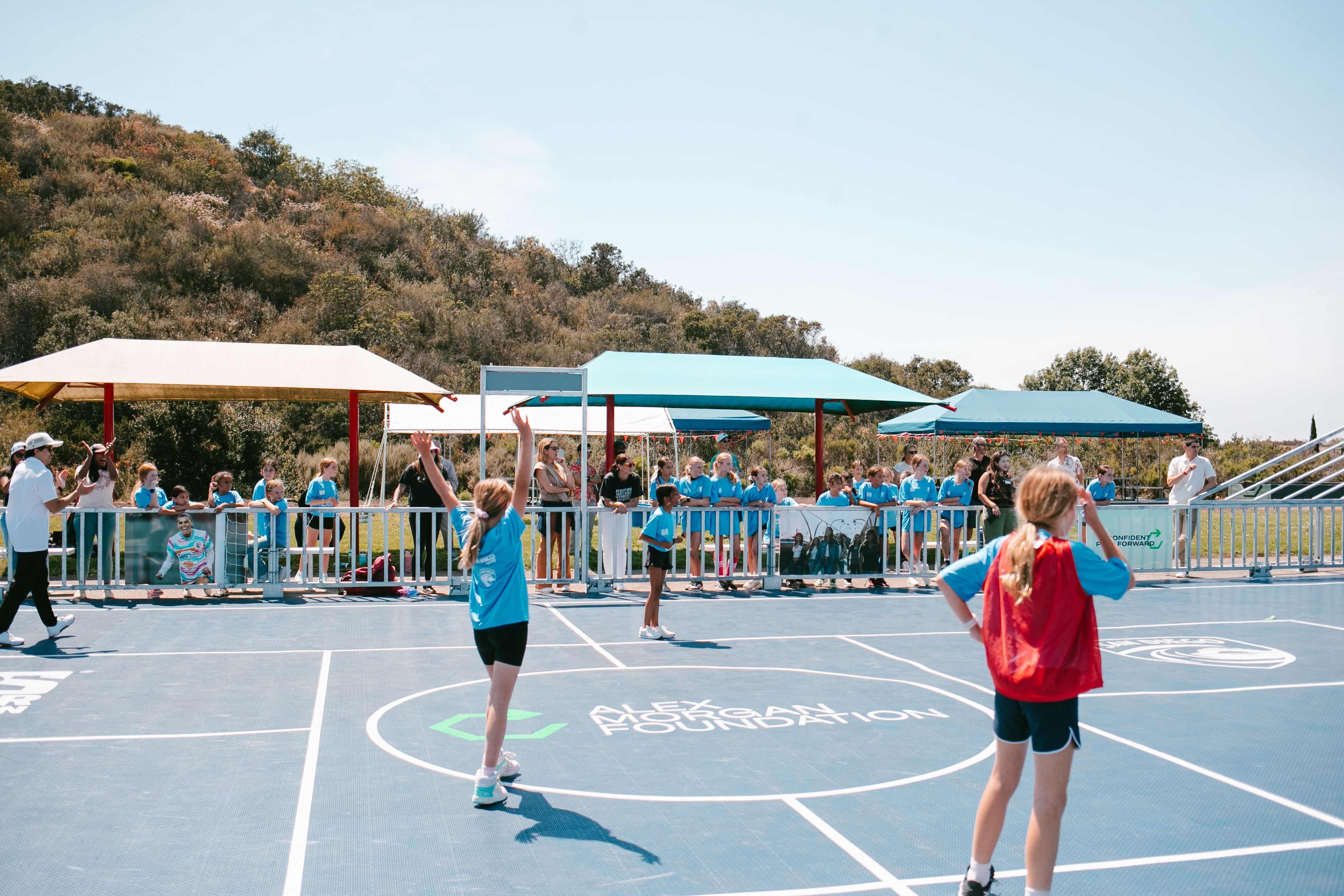Young girls play soccer on a blue court with "Alex Morgan Foundation" branding.