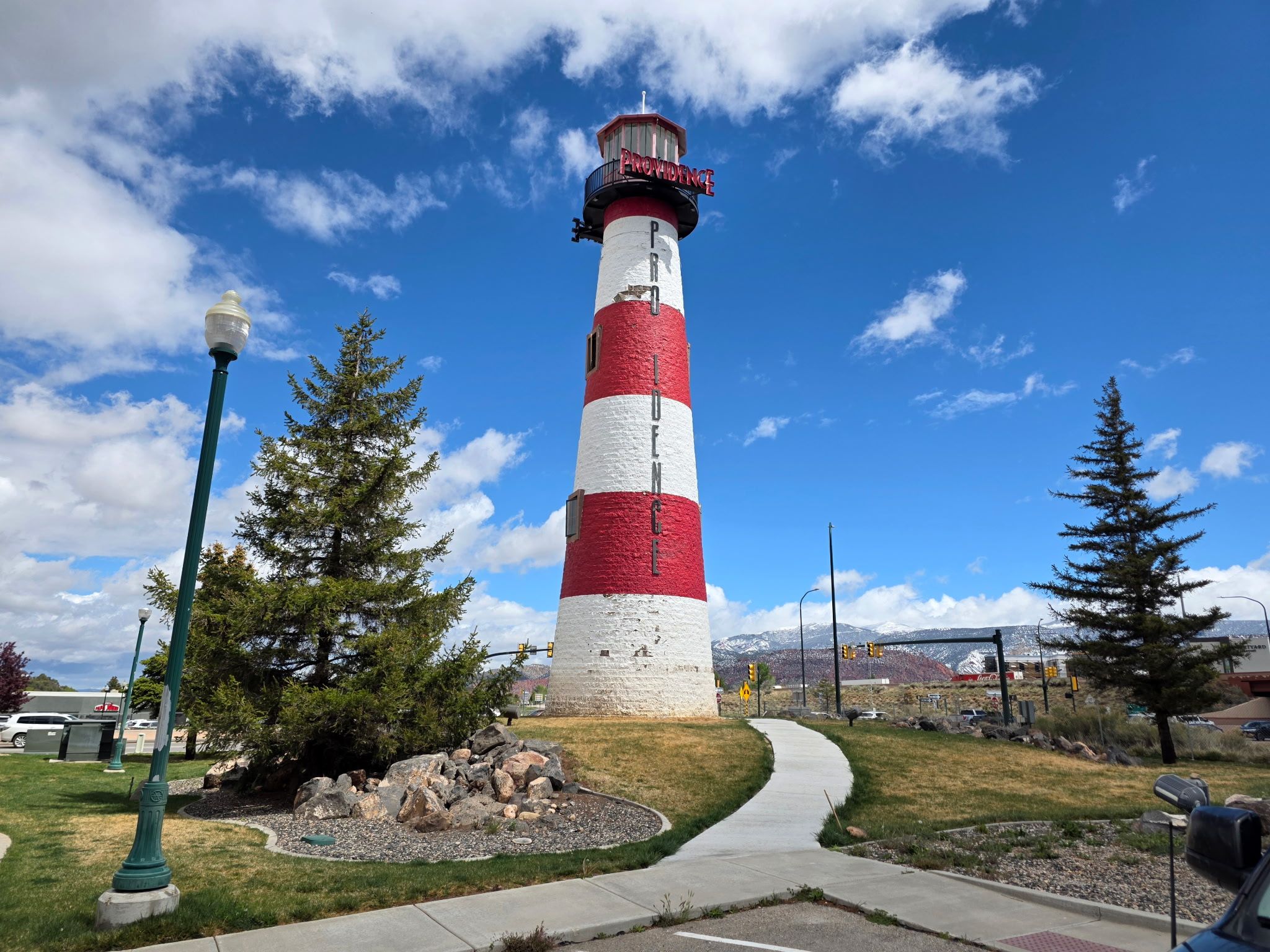 A red and white lighthouse stands on a grassy knoll with desert and snowy mountains in the distant background
