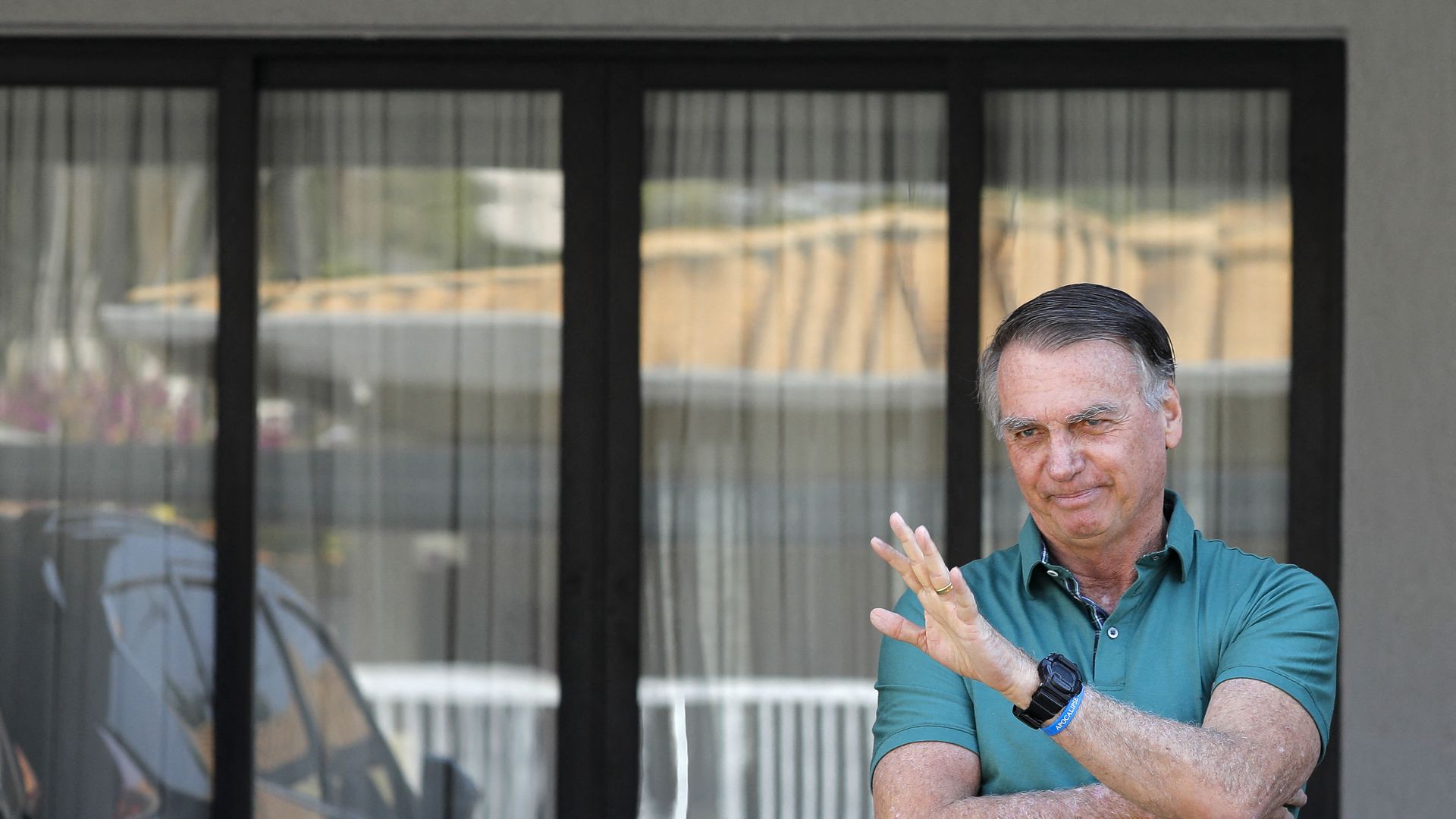 Former Brazilian President Jair Bolsonaro, wearing a green t-shirt, waves at his residence in Brasilia on September 11, 2025. 