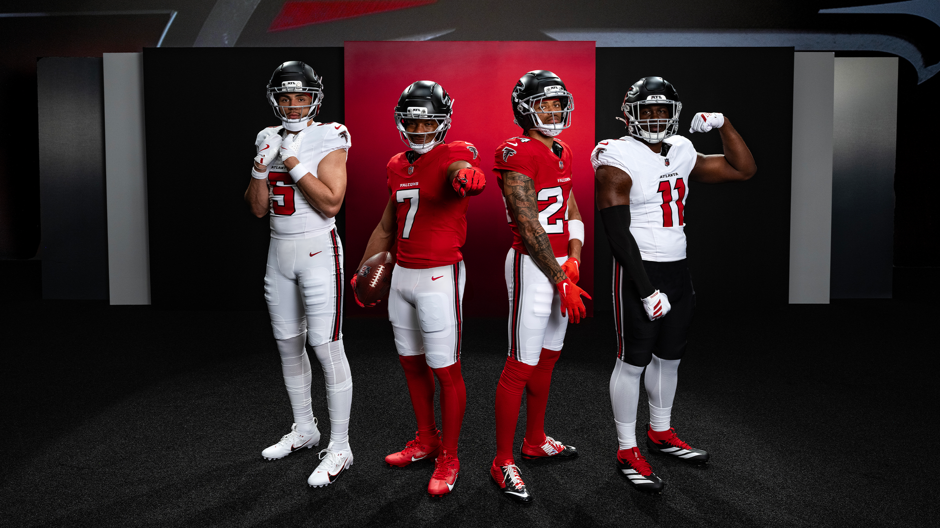 Four Atlanta Falcons football players pose in a studio wearing red and white uniforms; one holds a football, others strike poses in front of a dark backdrop with red panels.