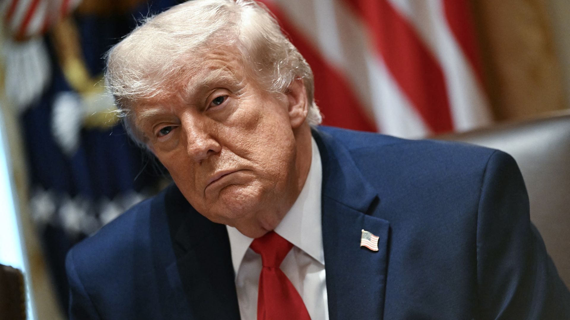 President Trump — wearing a dark blue suit, a white collared shirt, an American flag pin and a red tie — looks on during a Cabinet meeting.