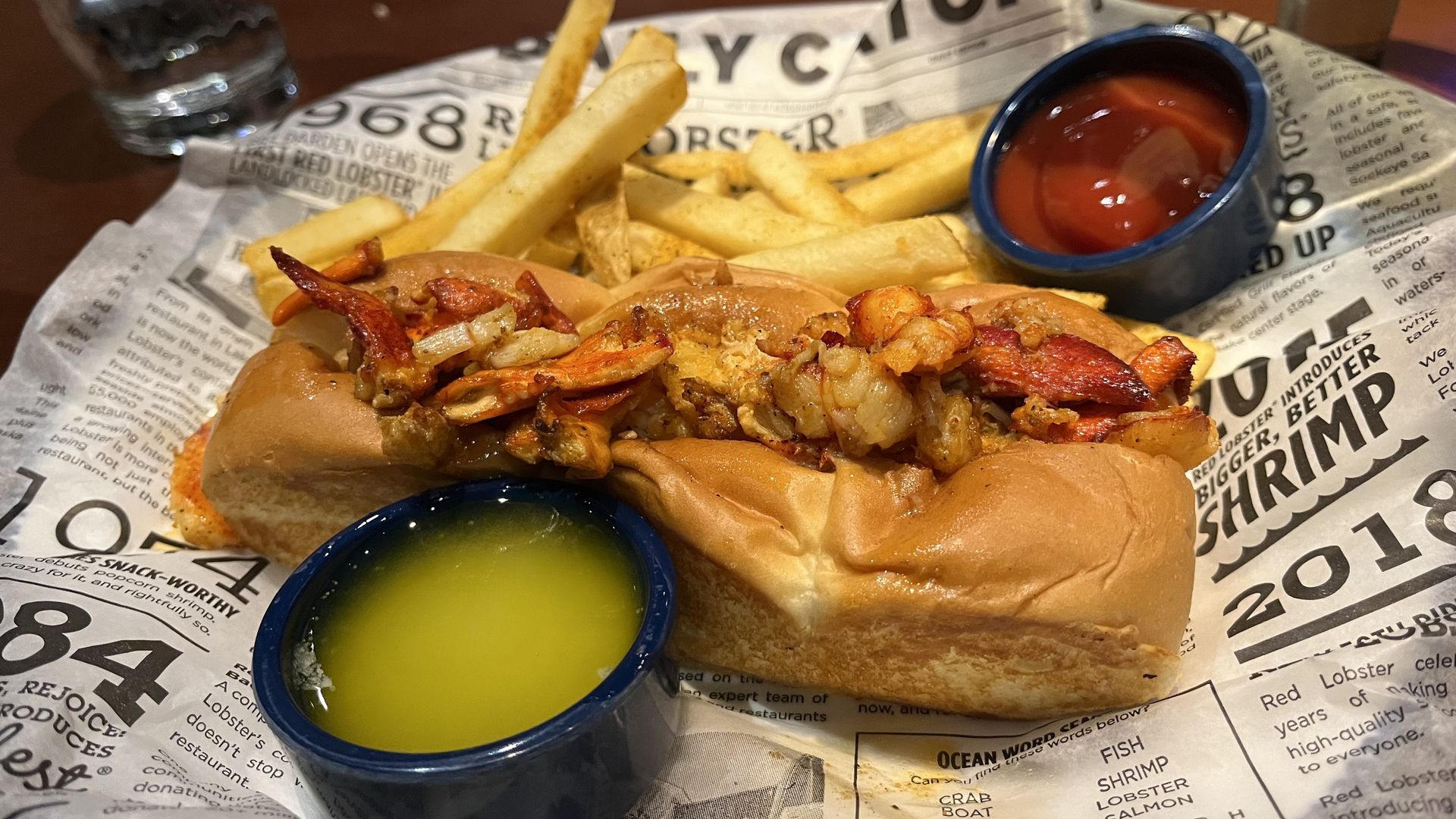 A lobster roll on a basket surrounded by butter and ketchup