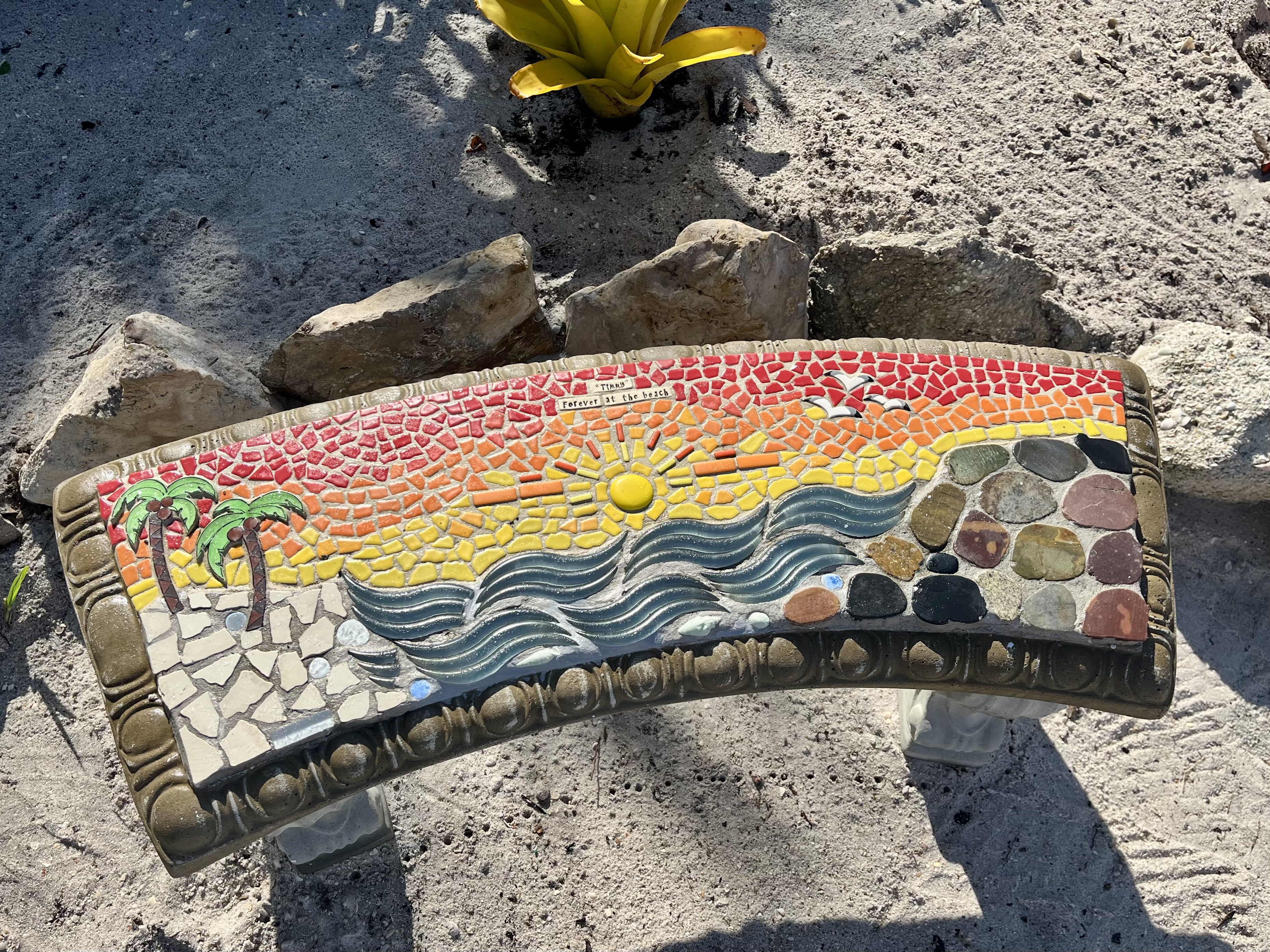 A bench with a mosaic of red, orange, yellow and blue tiles made to look like a sunset.