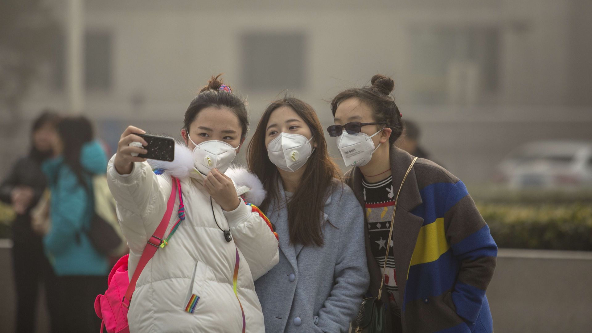 Young girls take selfie while wearing face mask.
