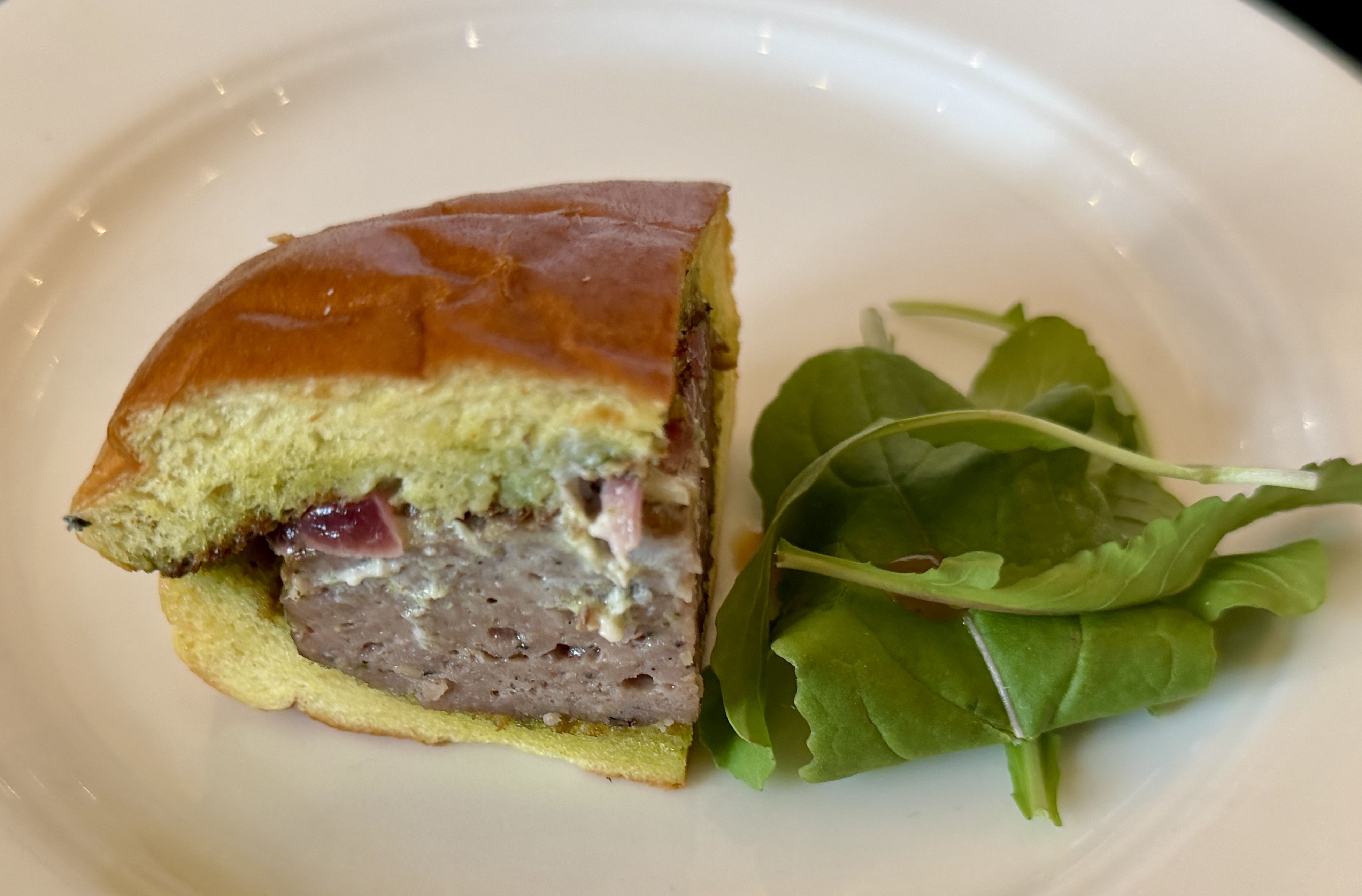 Plate with a thick slice of savory loaf sandwich, brown crust and pale yellow-green filling, beside fresh green salad leaves.