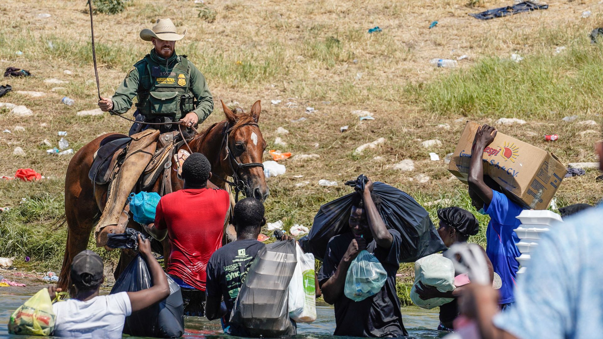 A United States Border Patrol agent on horseback uses the reins as he tries to stop Haitian migrants from entering an encampment on the banks of the Rio Grande