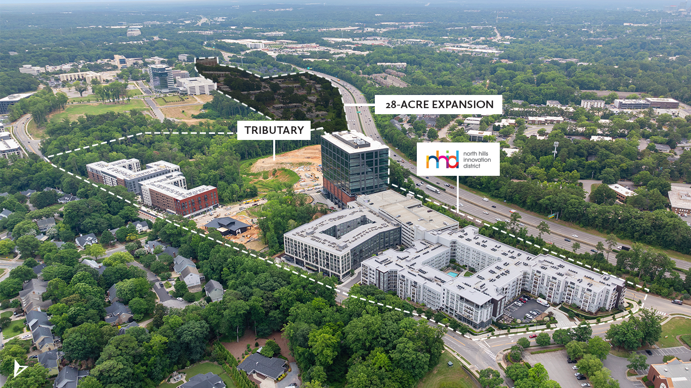 Aerial view of a modern campus with glass buildings, roads, and green trees. Dashed lines mark a labeled TRIBUTARY and a 28-acre expansion; logo reads North Hills Innovation District near the highway.