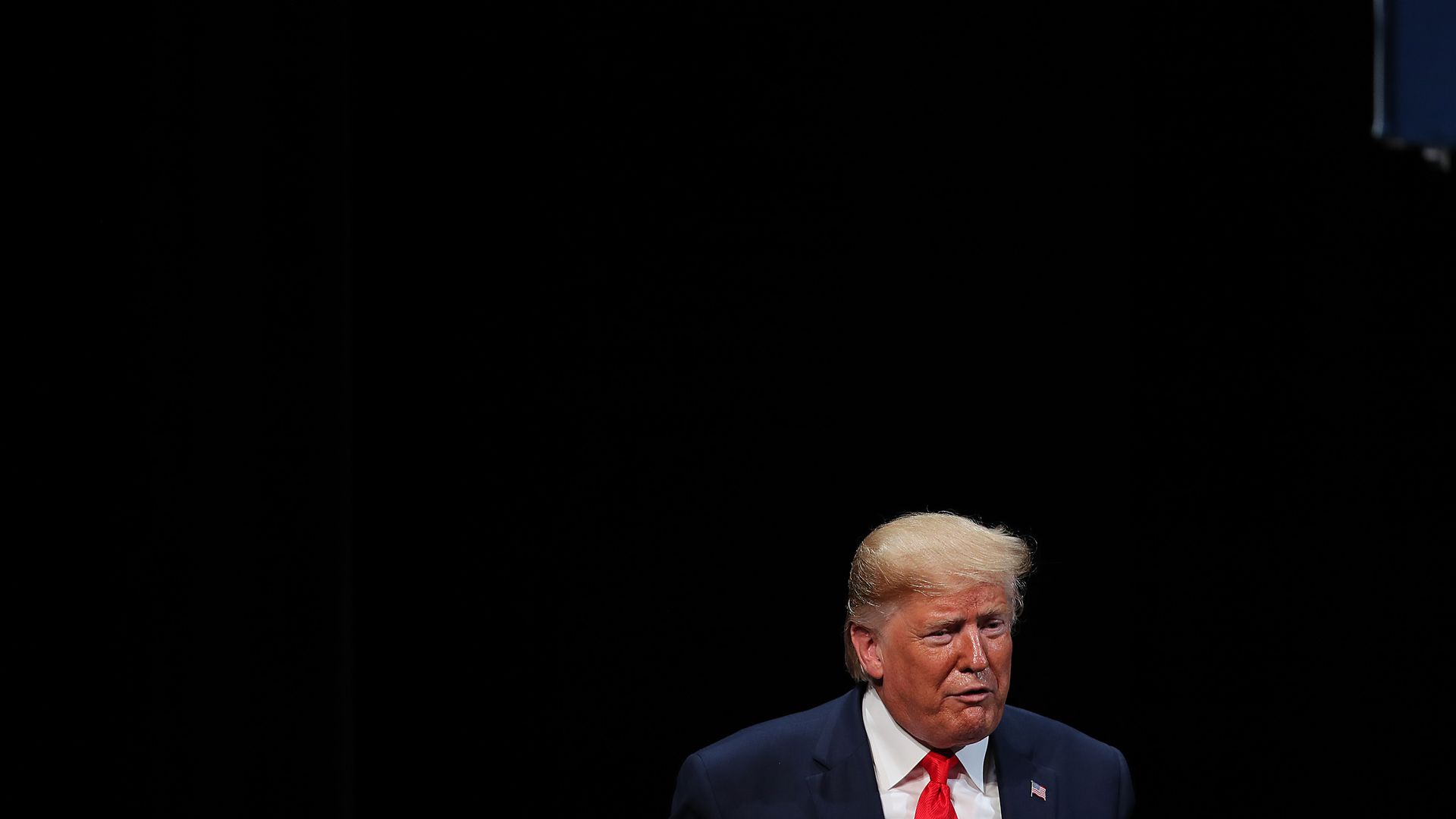 In this image, Trump wears a tie and stands. Only the top of his torso is visible.