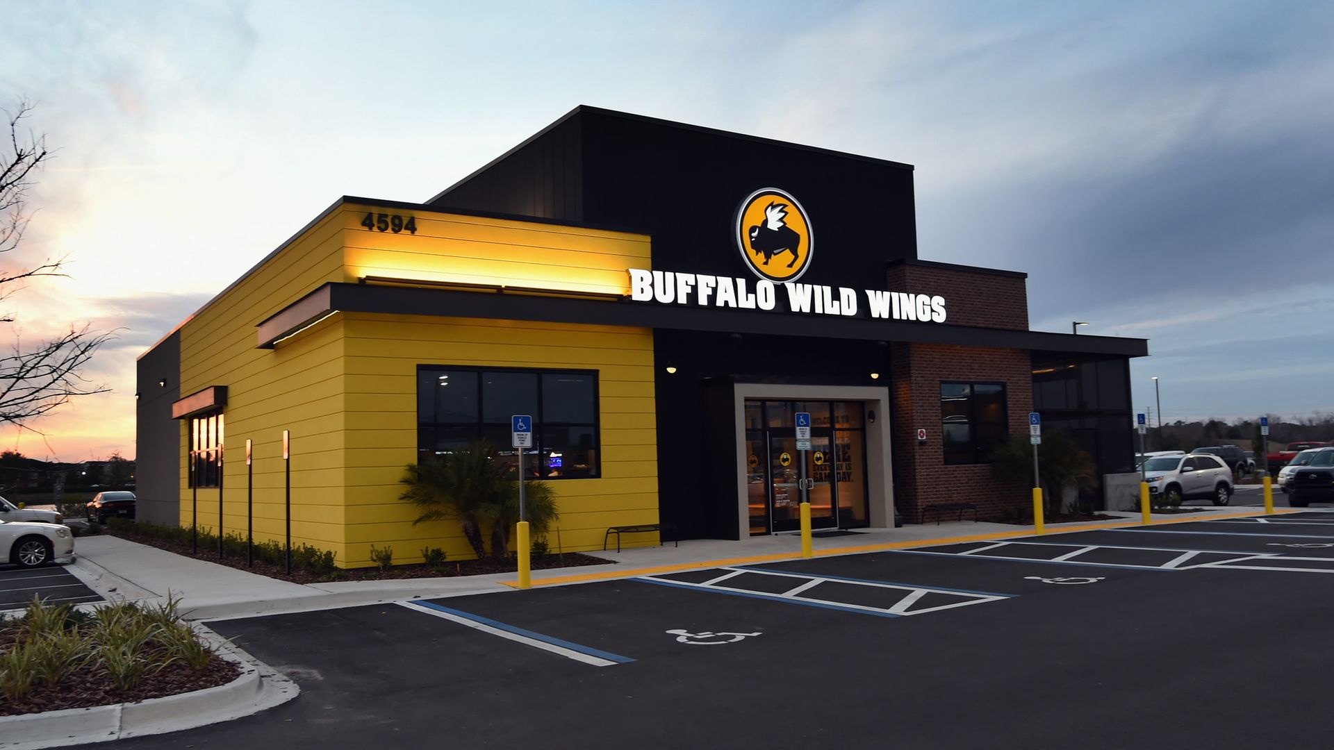 Exterior of a Buffalo Wild Wings restaurant at sunset with a black and yellow facade, visible logo, under a cloudy sky.