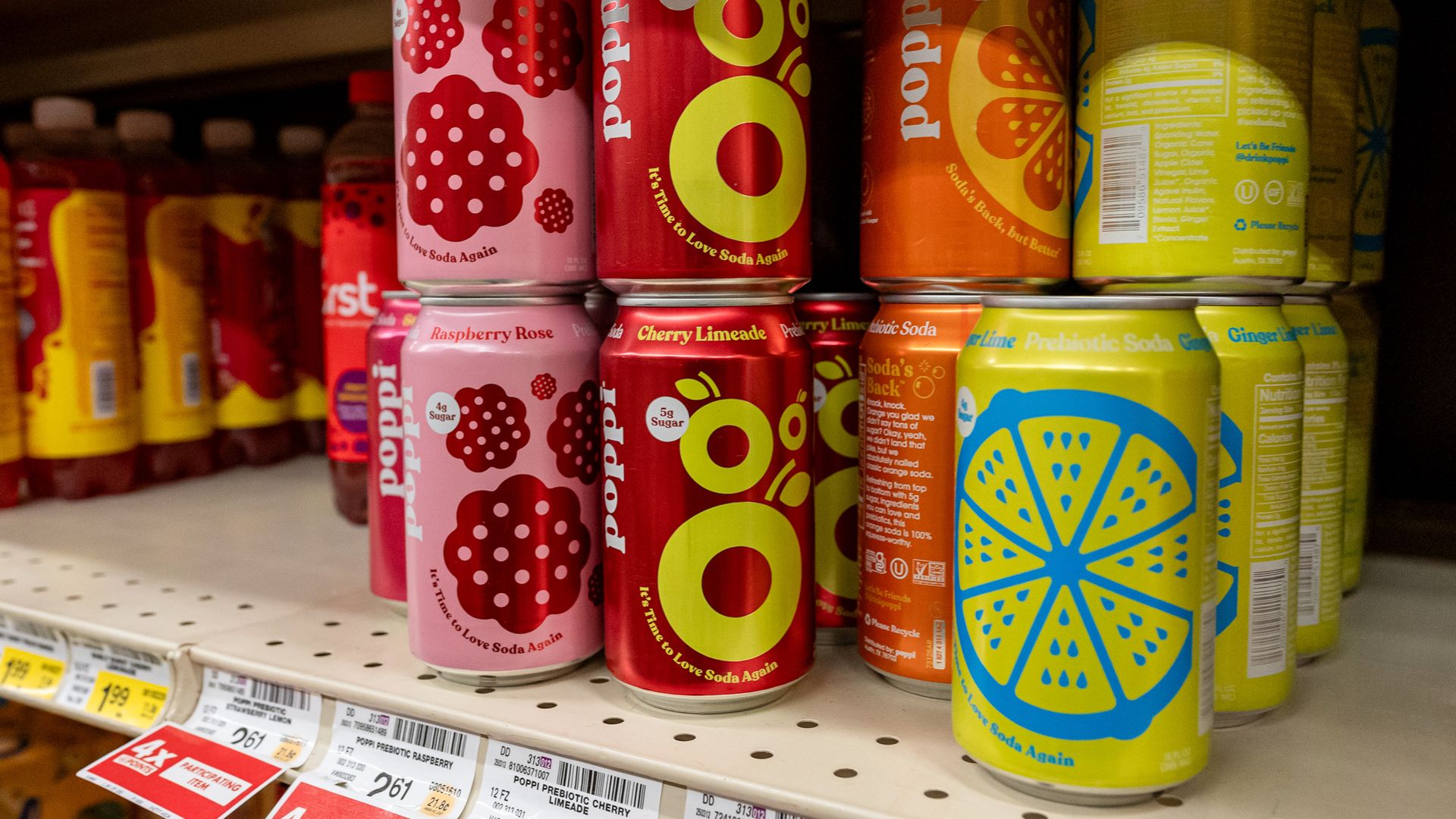 Pink, red, orange and yellow cans of Poppi soda on a grocery store shelf.