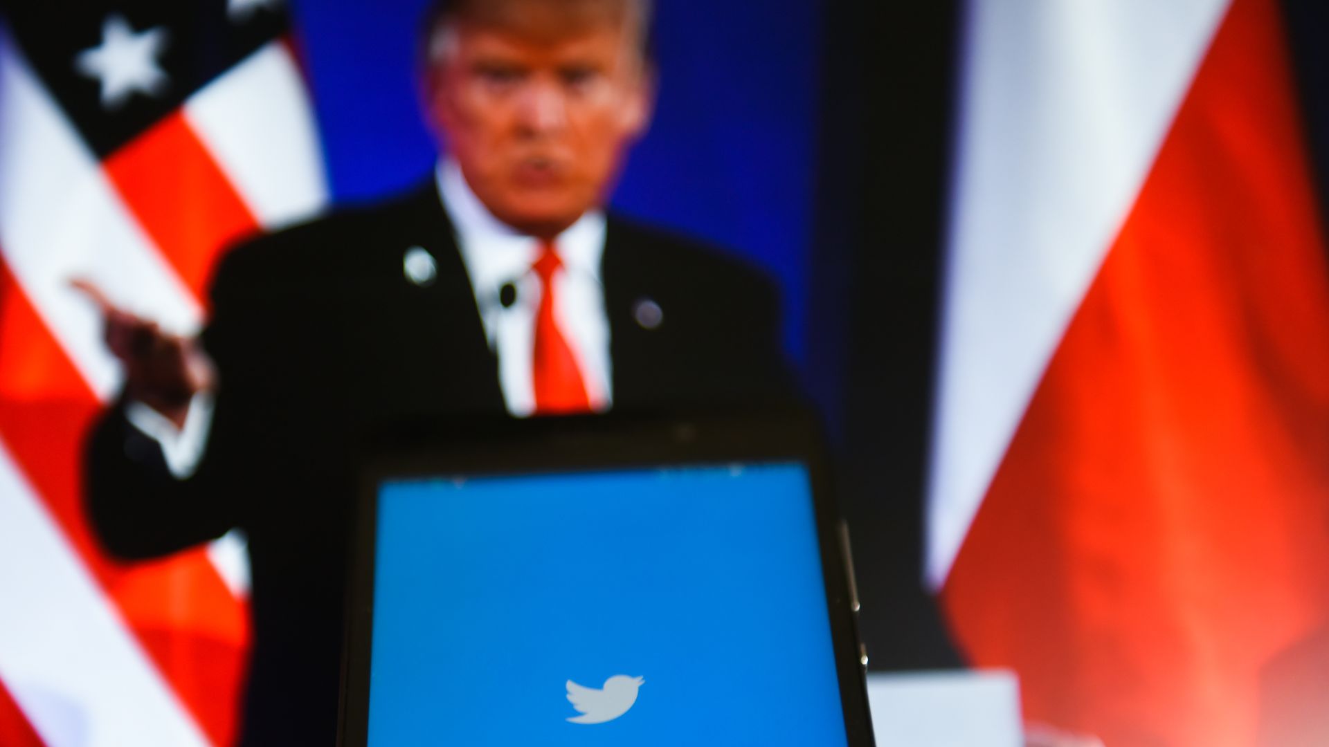The twitter app on a phone with Donald Trump in the background.