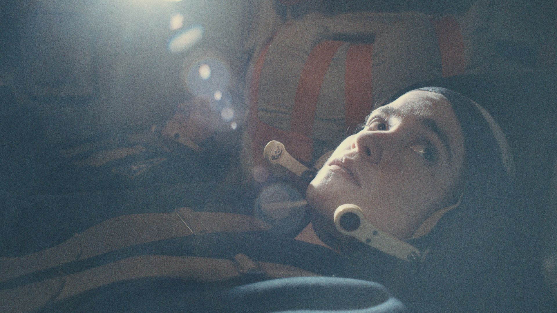 Alice Englert lying down inside what appears to be a spaceship. She's wearing a headpiece and chest belt.