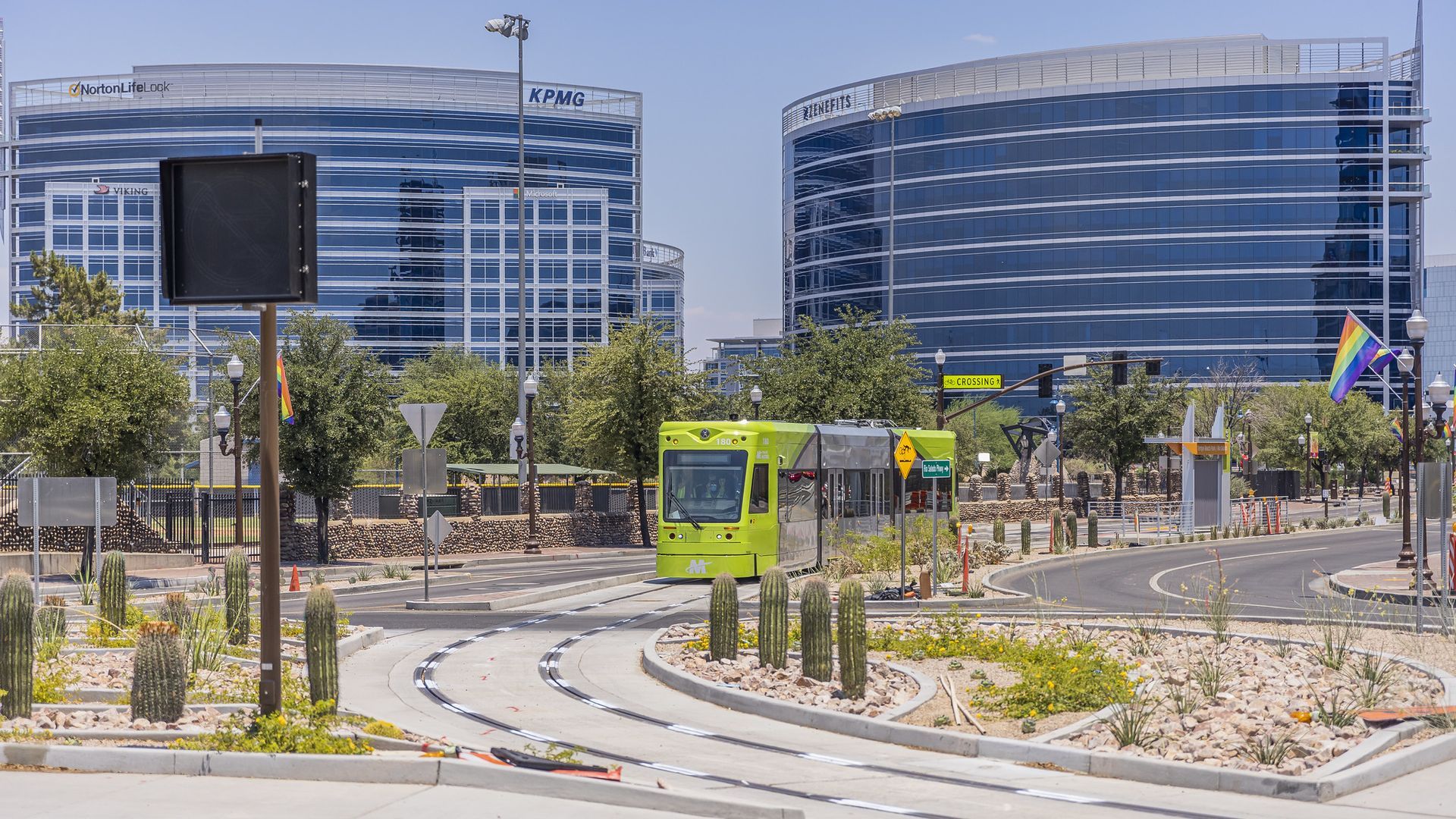 A neon green streetcar on a rail in front of two office buildings. 