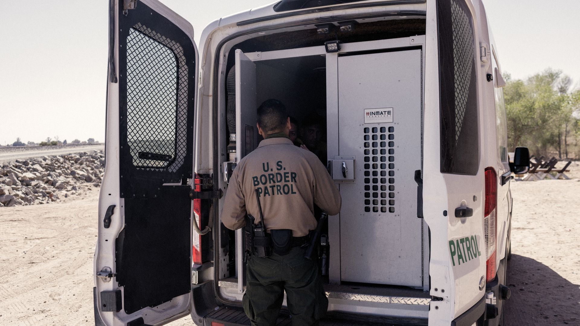 U.S. Customs and Border Protection officer speaks with migrants seeking asylum inside a vehicle before they are transferred to temporary shelters in Yuma, Arizona, U.S., on Monday, Feb. 21, 2022. 