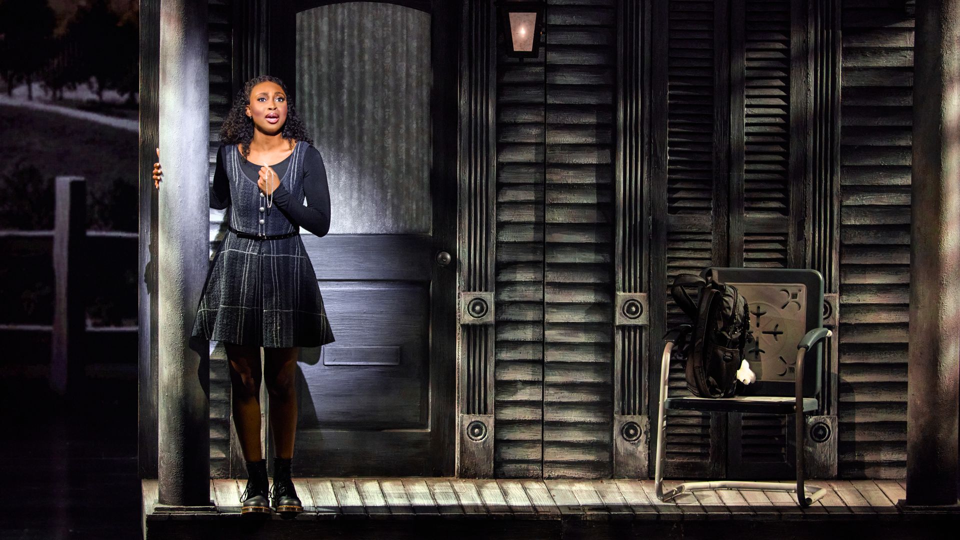 A woman stands on a theater stage front porch singing 