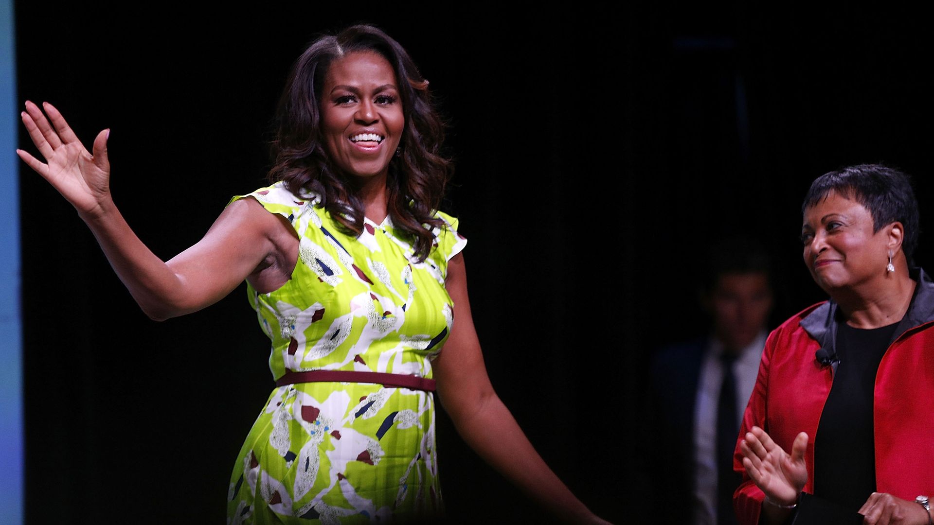 Michelle Obama waving on stage in a green flower=print dress.