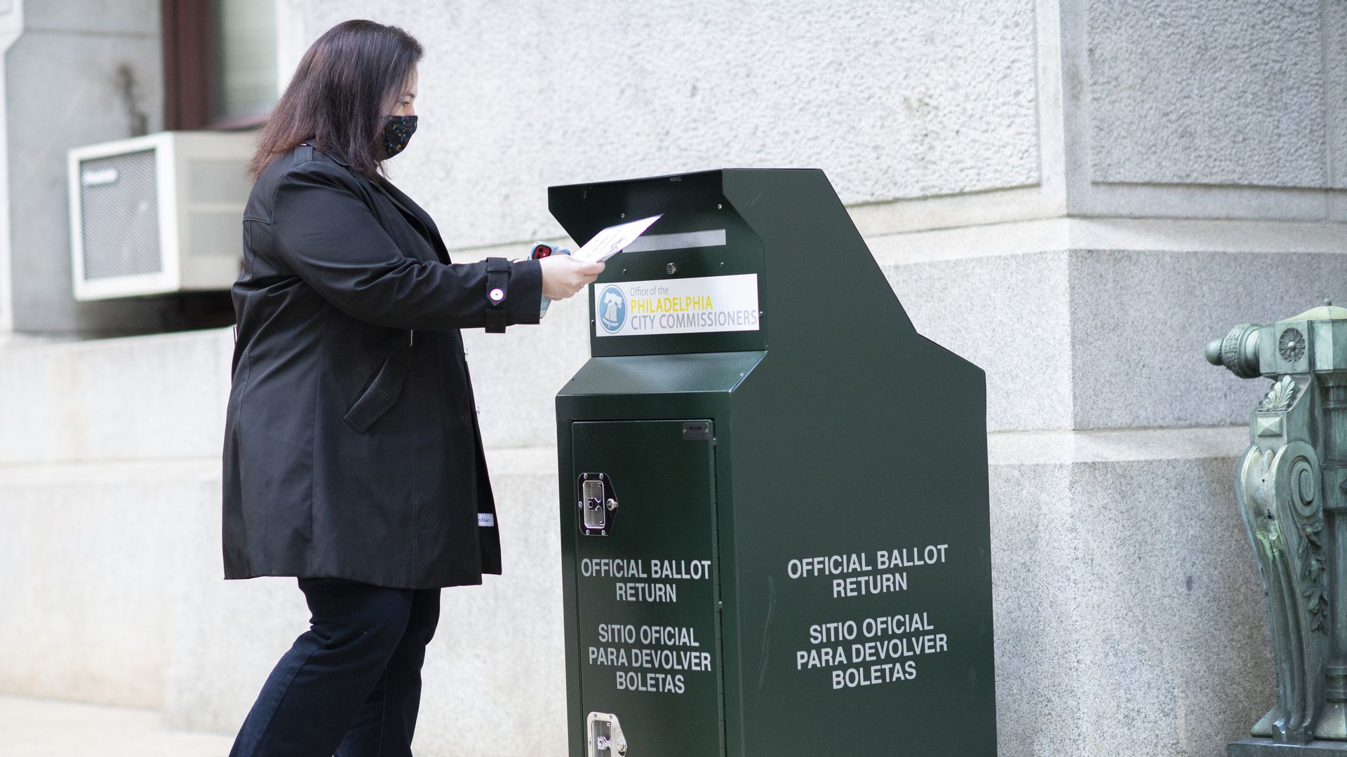 Picture of a woman outside dropping off  her ballot in a green official ballot box in Philadelphia