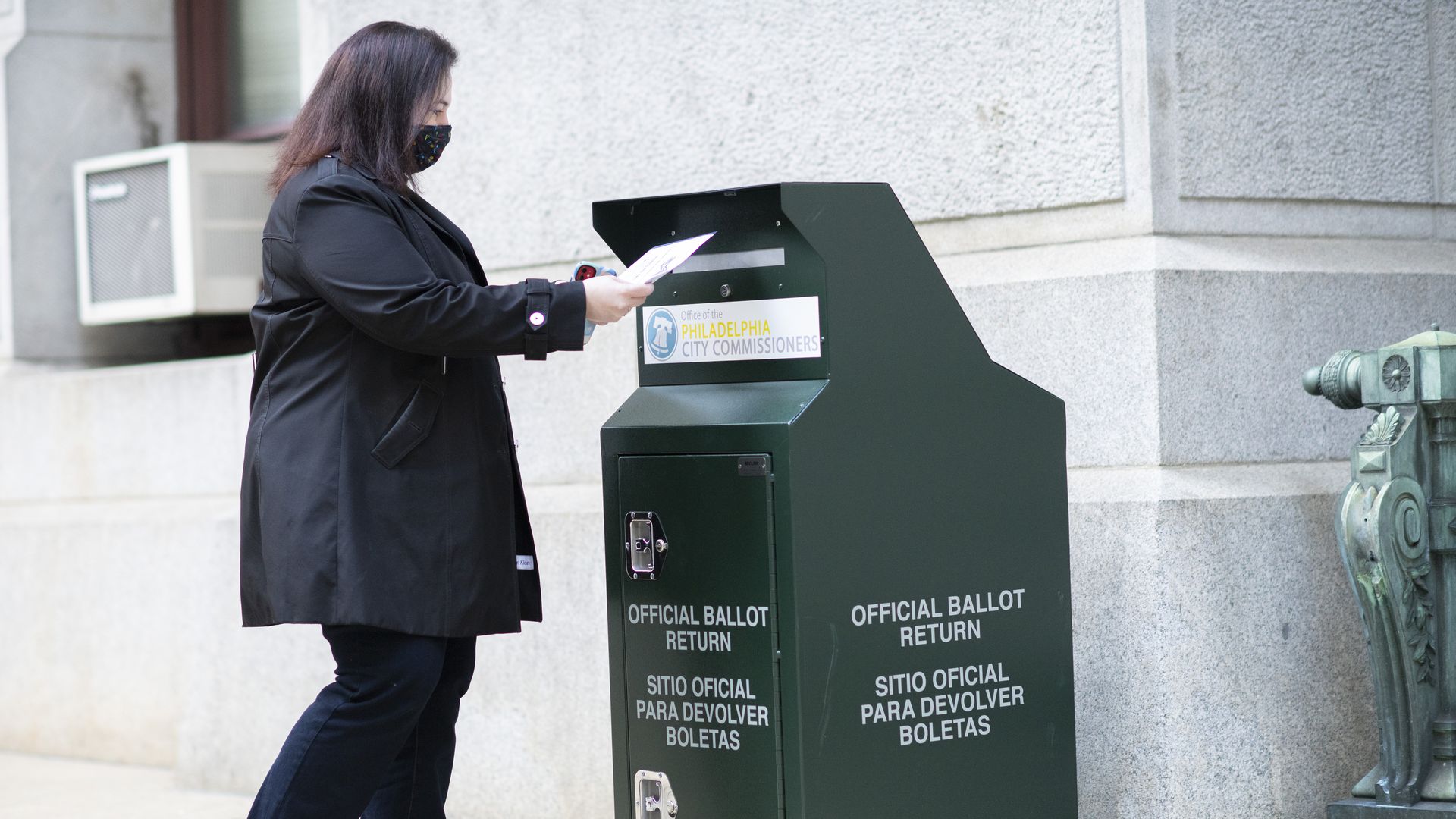Picture of a woman outside dropping off her ballot in a green official ballot box in Philadelphia