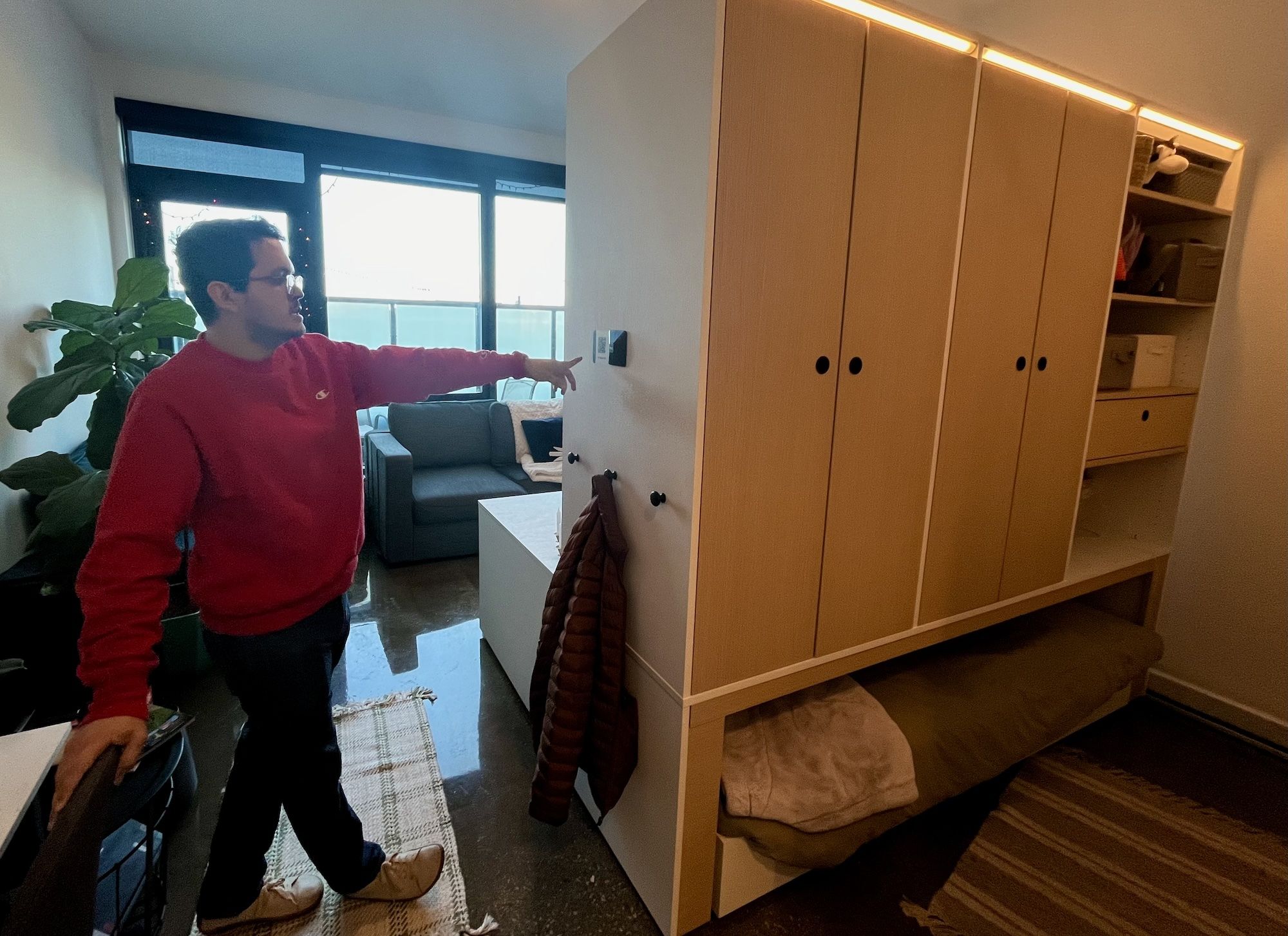 Man points to side of wood cabinet with a bed below it.