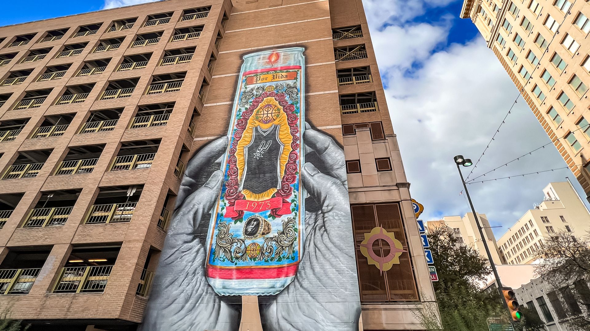 A mural depicting hands holding a Spurs-themed vela is painted on a multi-story parking garage.