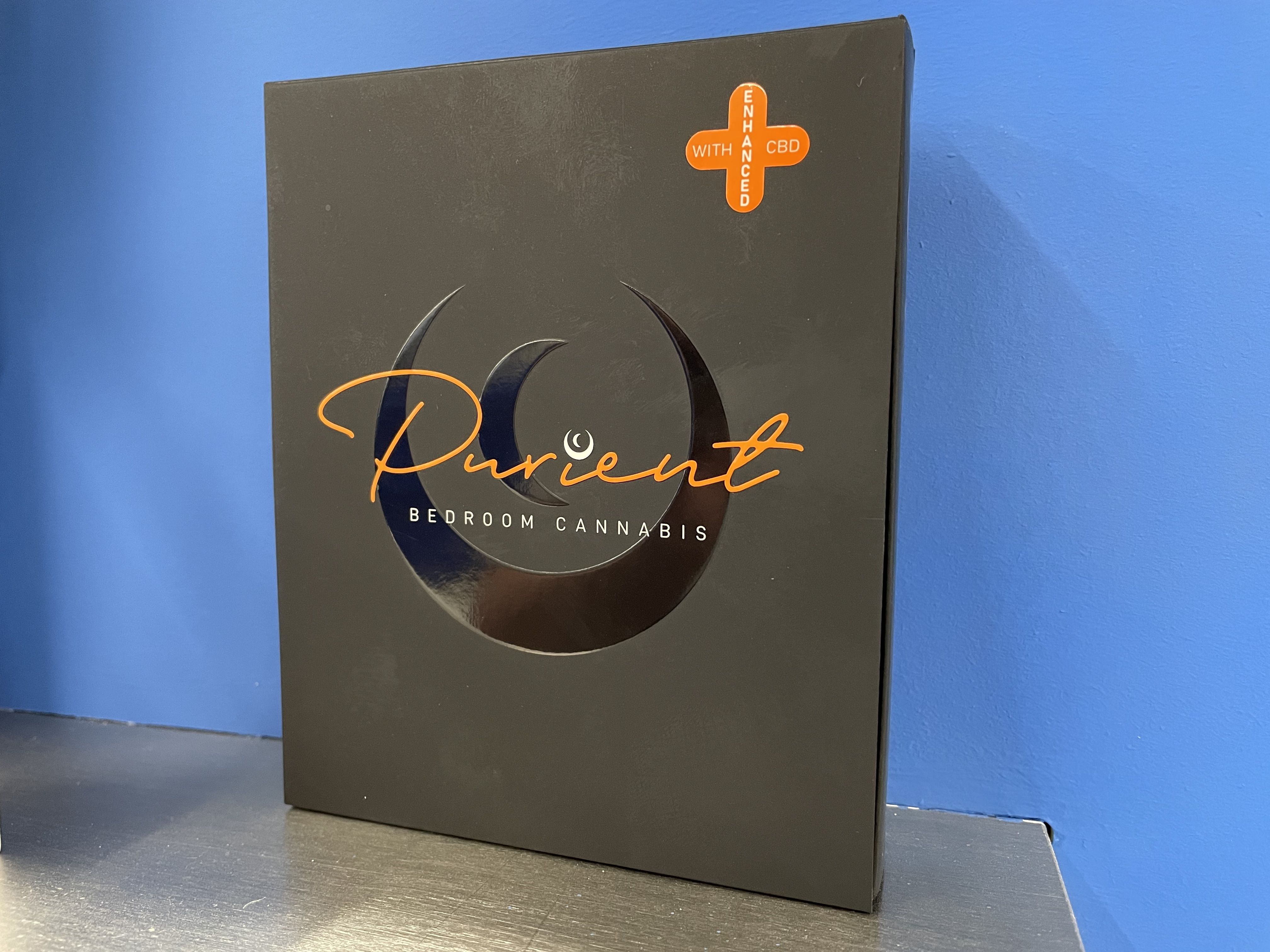 A black box with the words Purient Bedroom Cannabis in orange sits on a blue display wall.