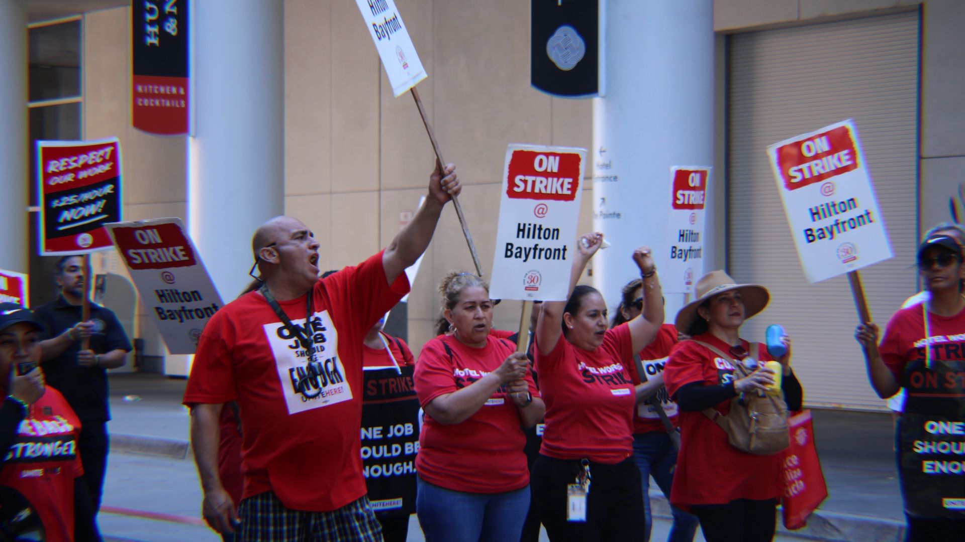 Hotel workers in red tee shirts on strike with picket signs. 