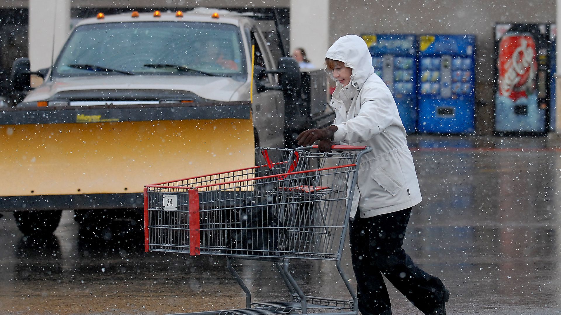 A person wheels a shopping cart through a stormy parking lot