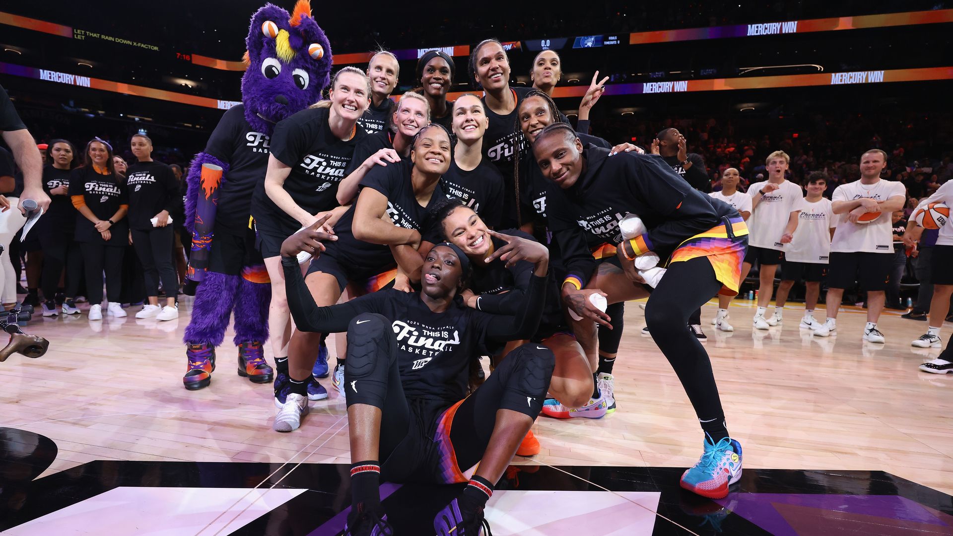 A women's basketball team wearing "Finals" t-shirts poses for a photo with a mascot. 