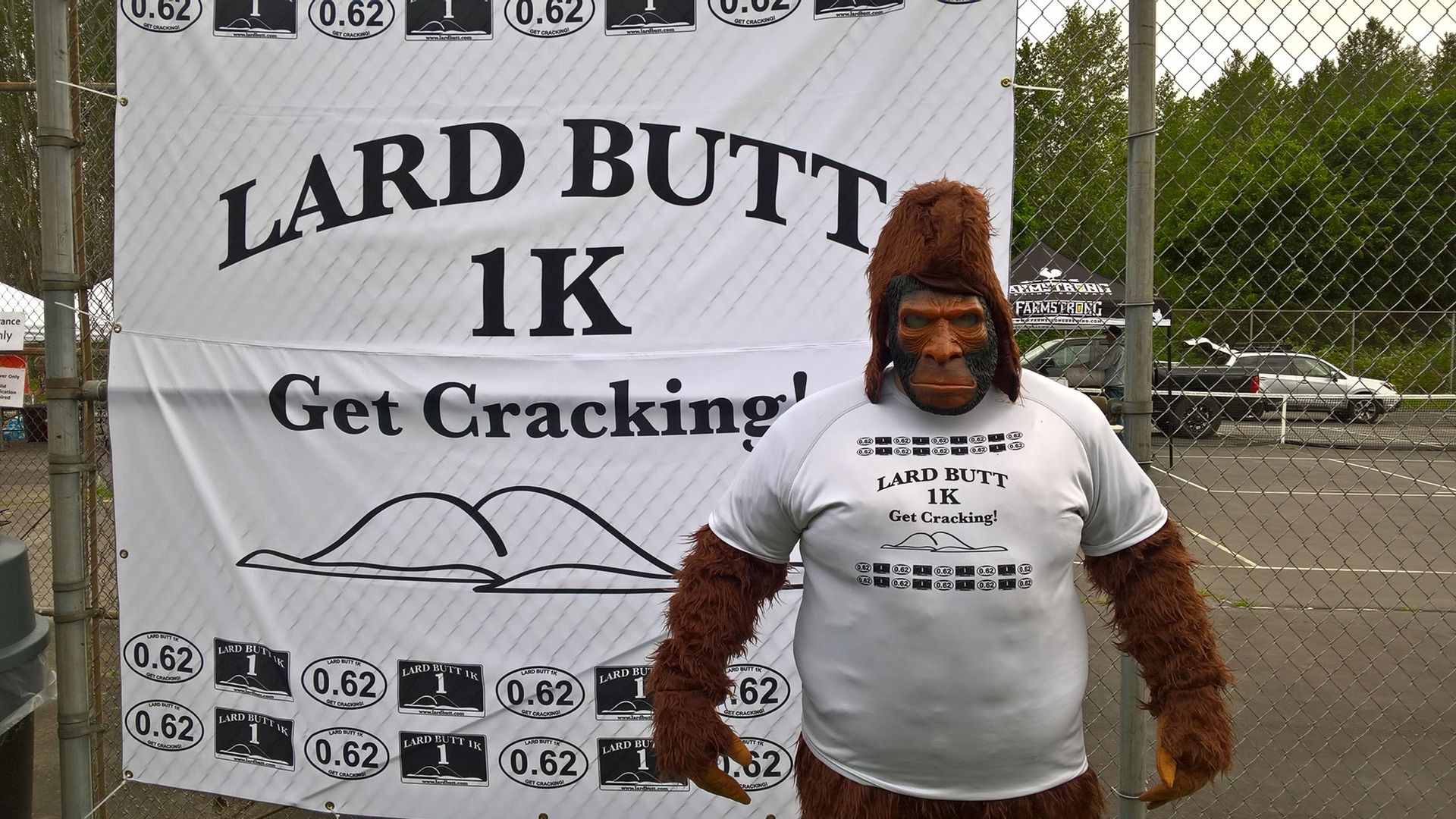 A person dressed up as a sasquatch in front of an poster for an upcoming 1k run.
