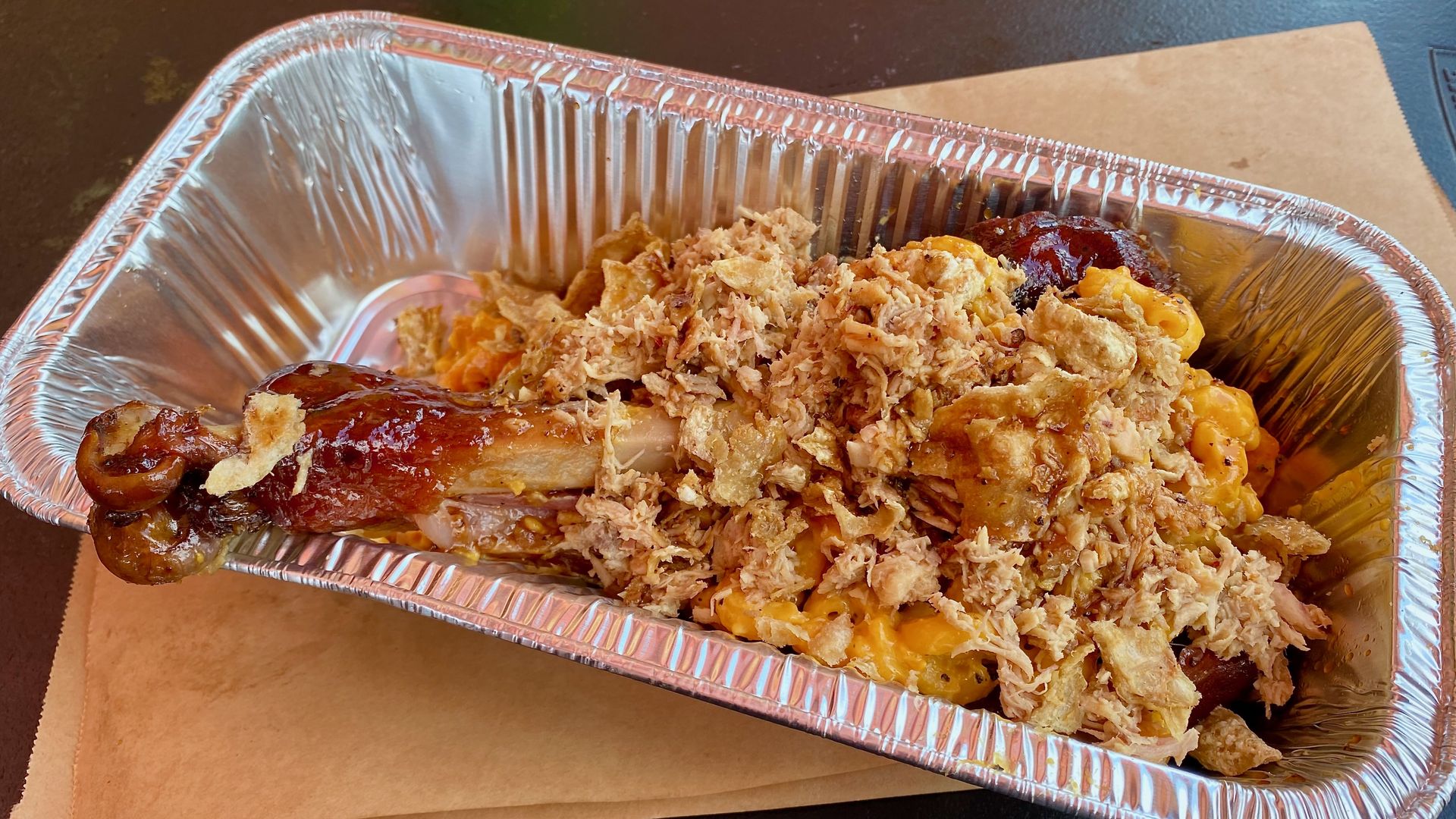 A turkey leg in a foil pan topped with mac and cheese and shredded turkey