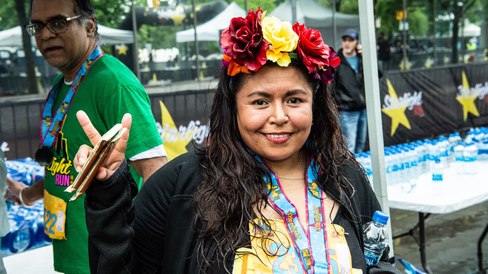 A woman with big red and yellow roses in her hair flashes a peace sign at the camera.
