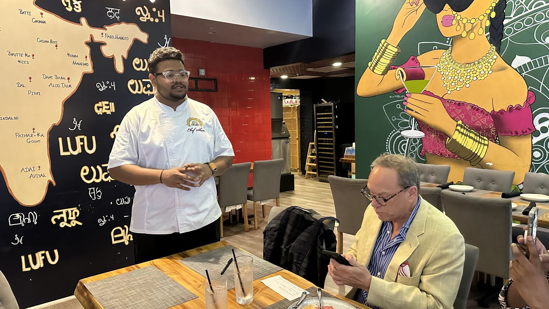 A man in a chef's coat speaks to a table of diners.